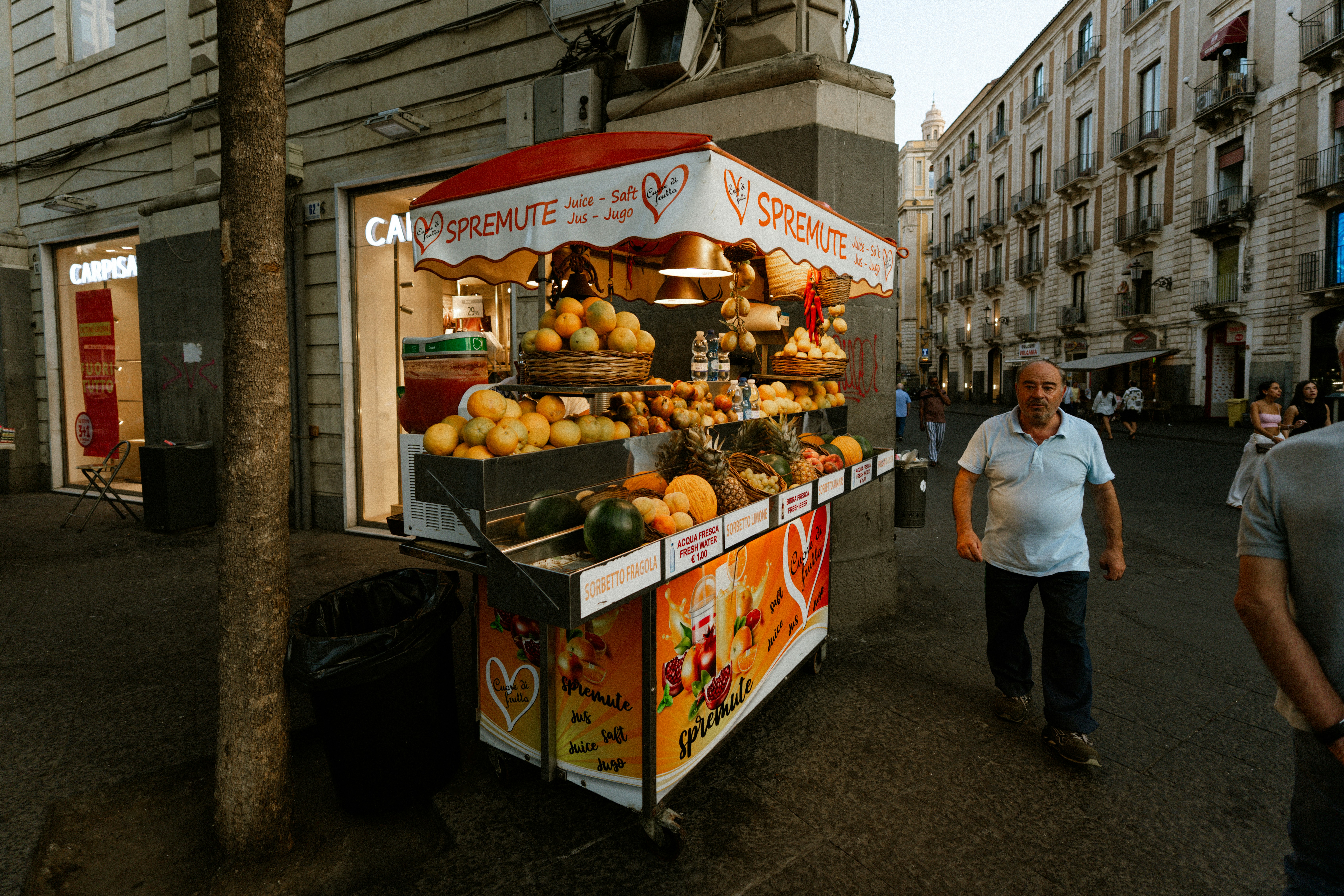 Man walks past a fruit stand on a city street.