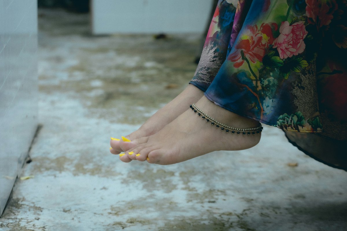 Pés com tornozeleira dourada e verniz amarelo nas unhas