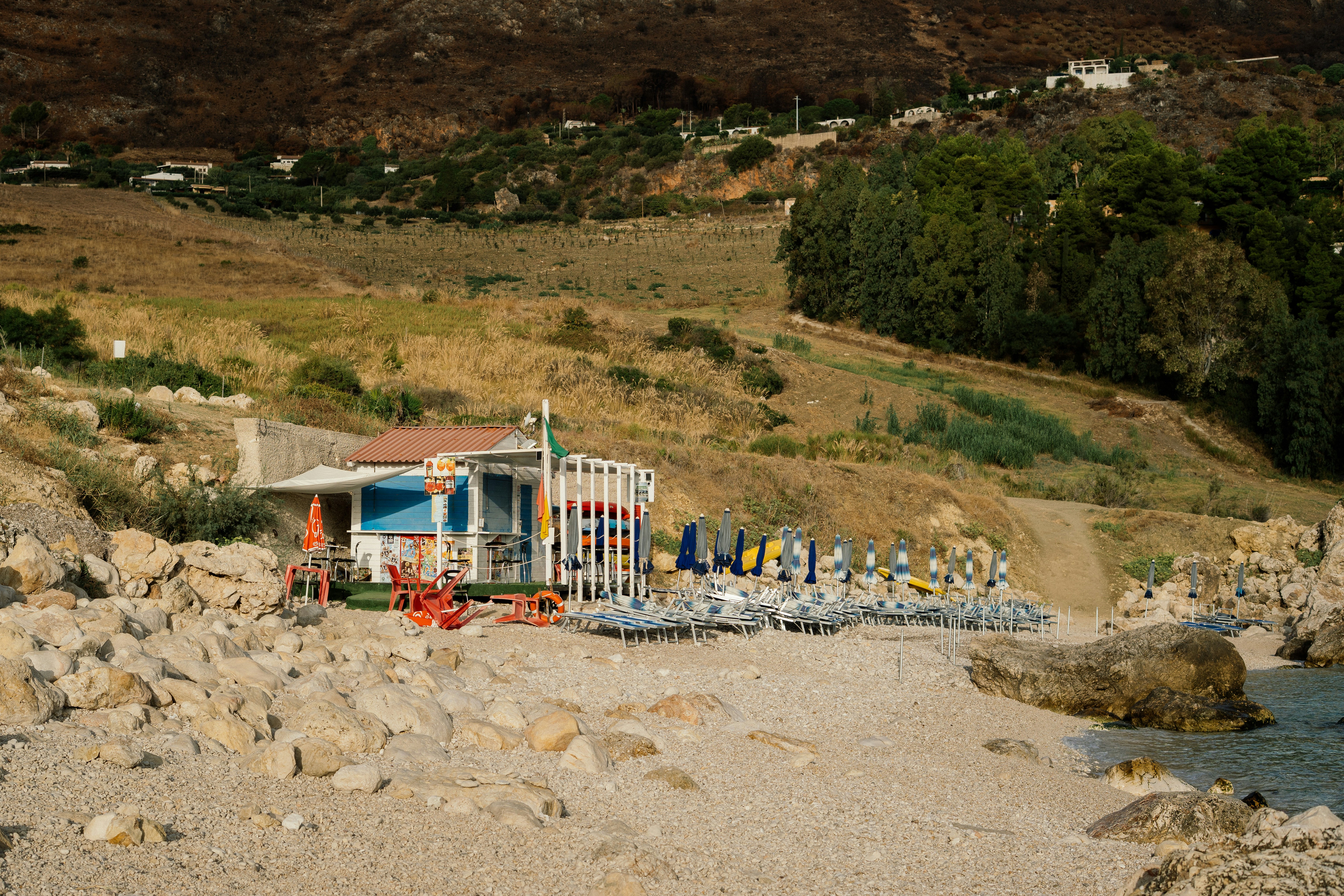 Small beachside cafe with lounge chairs on rocky shore.