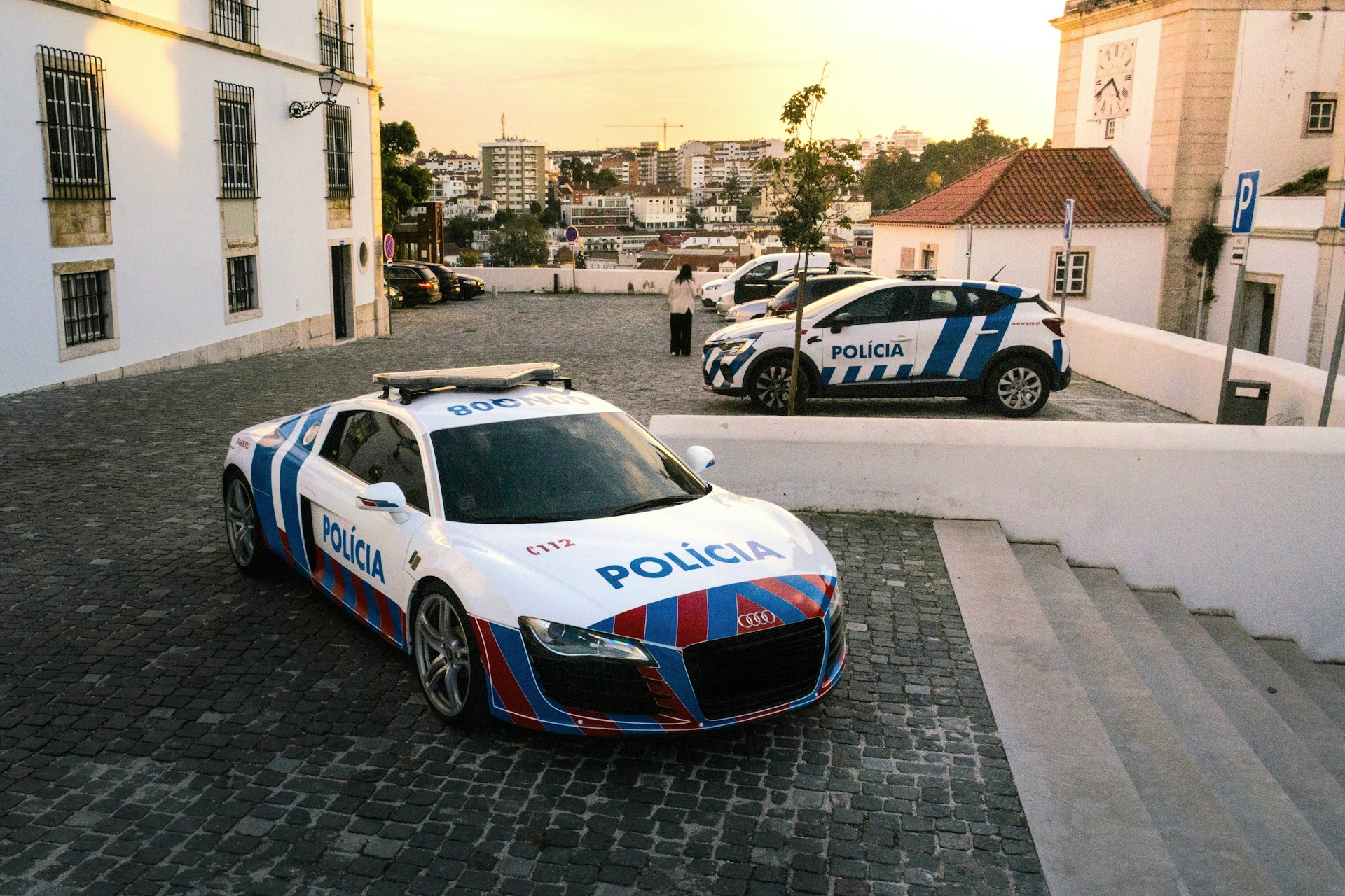 Two portuguese police cars parked on cobblestone street.