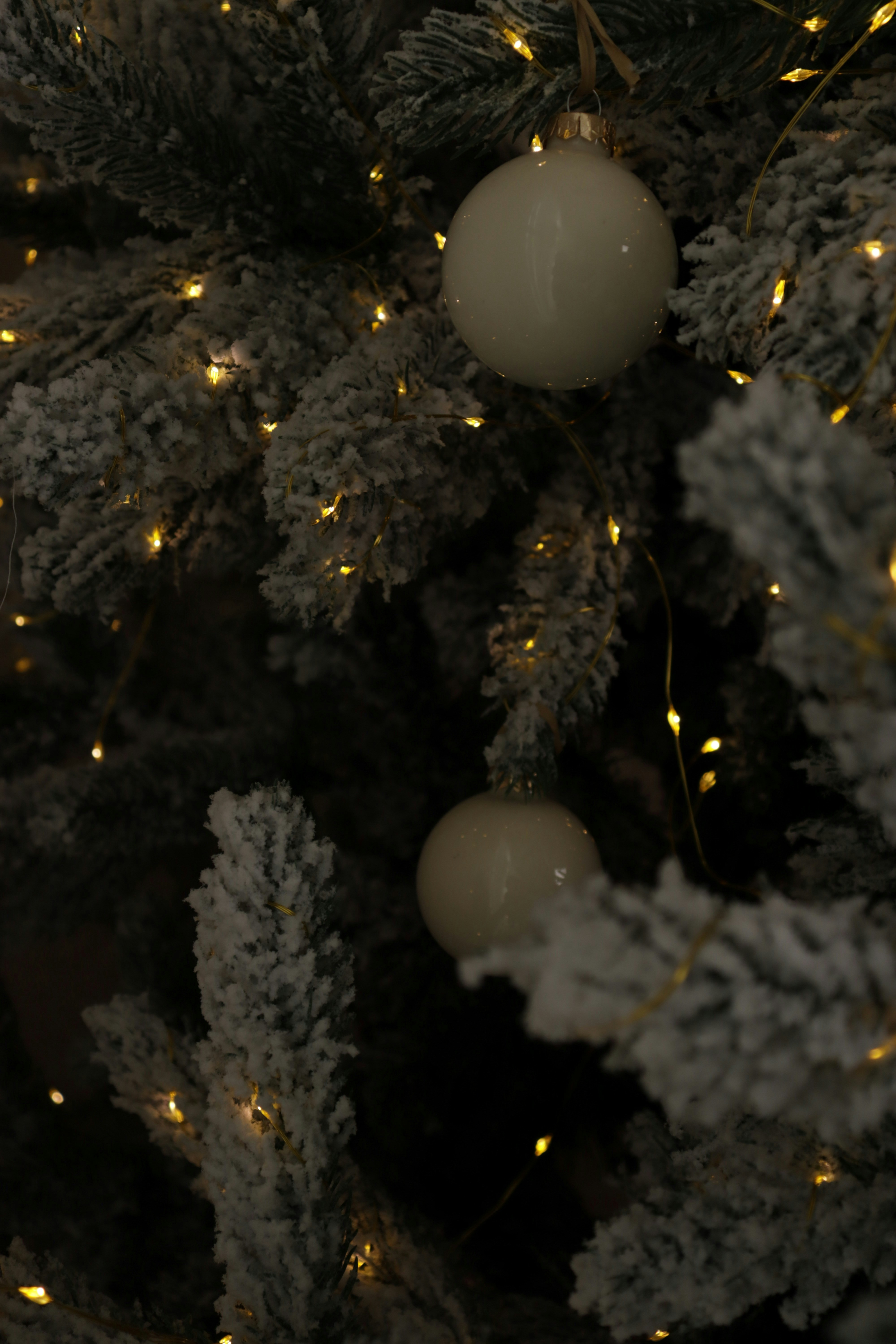 White ornaments on a decorated christmas tree with lights.