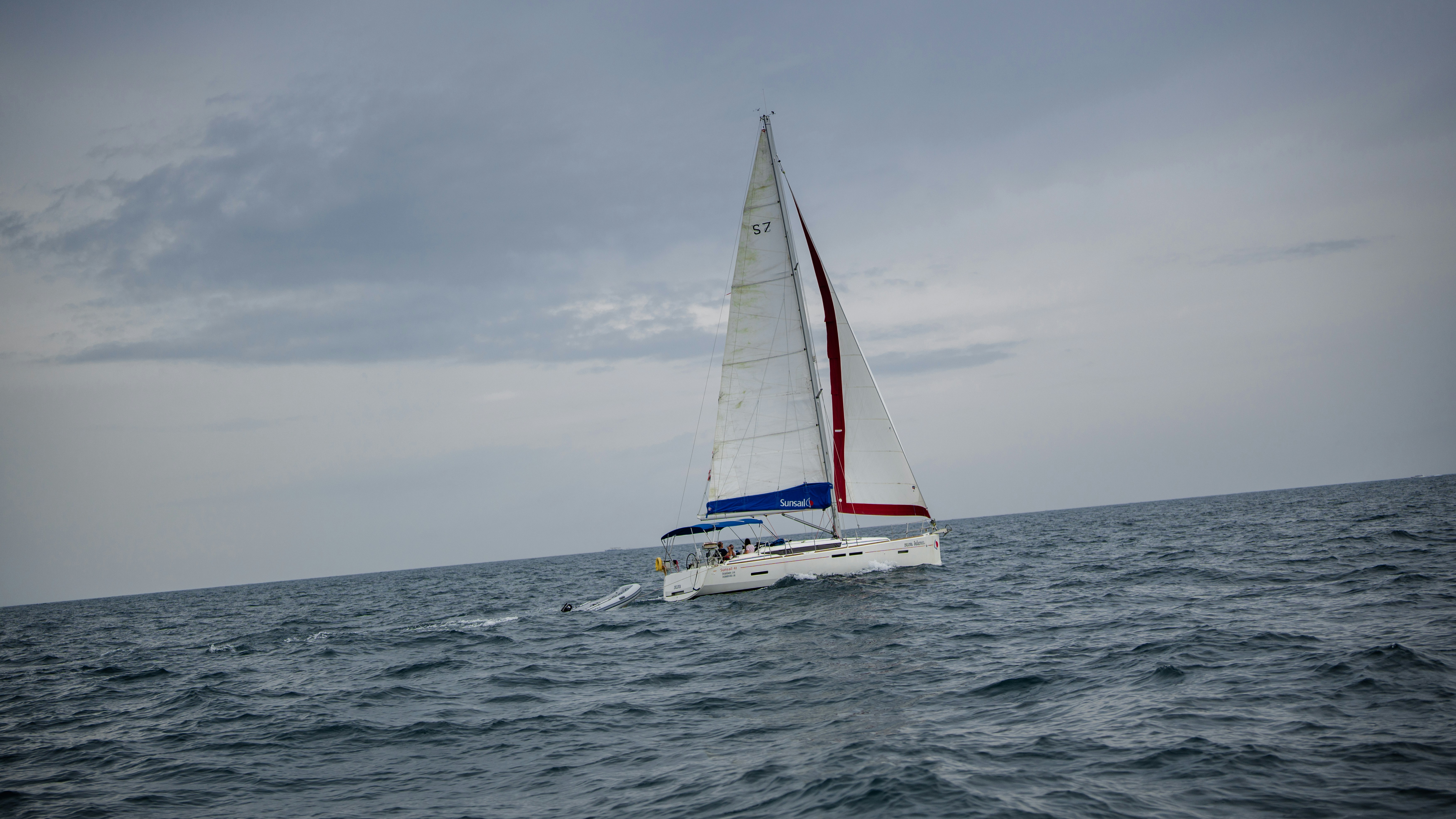 A white sailboat sailing on a choppy blue ocean