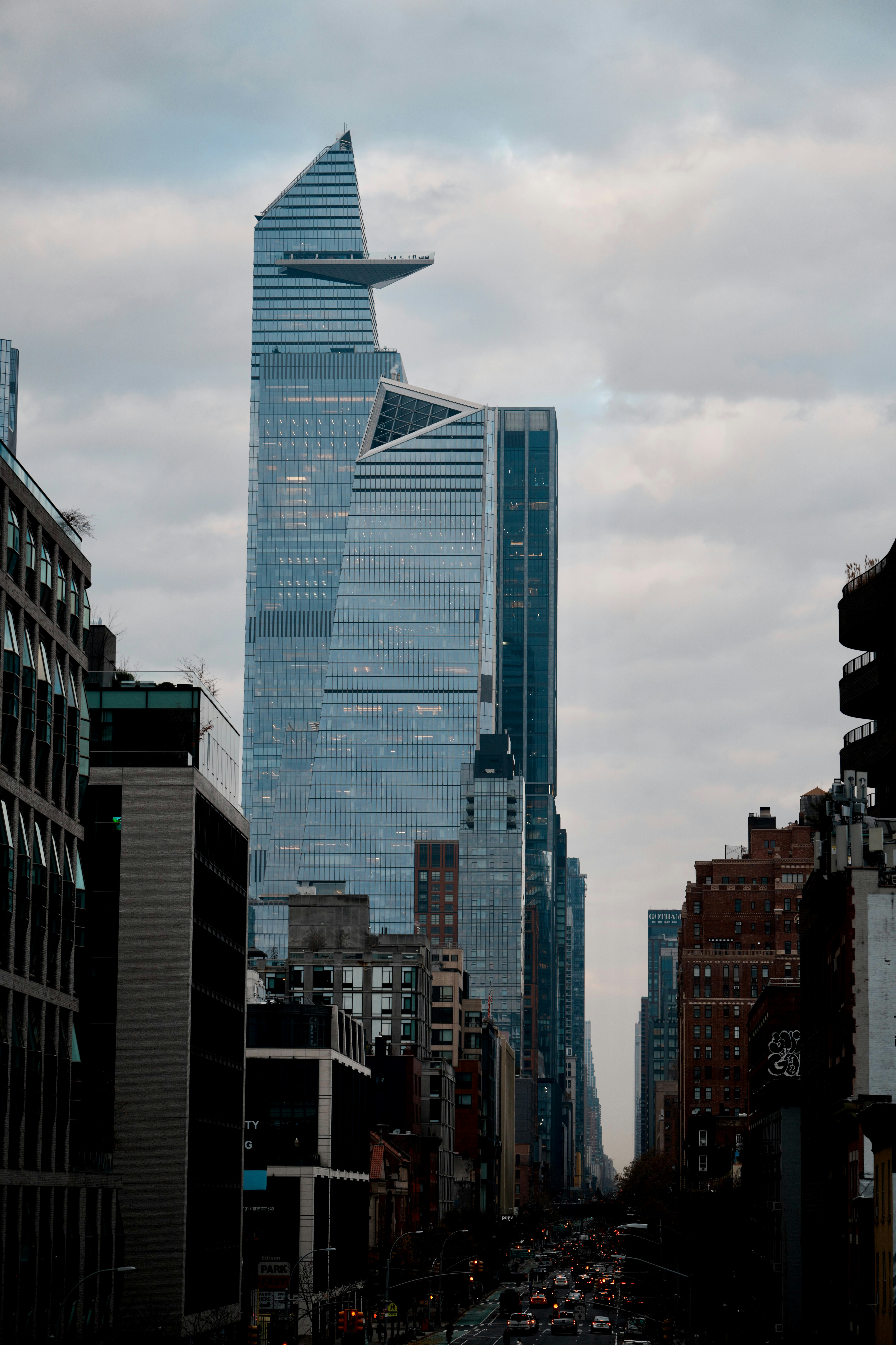 Modern skyscrapers line a city street under cloudy skies.