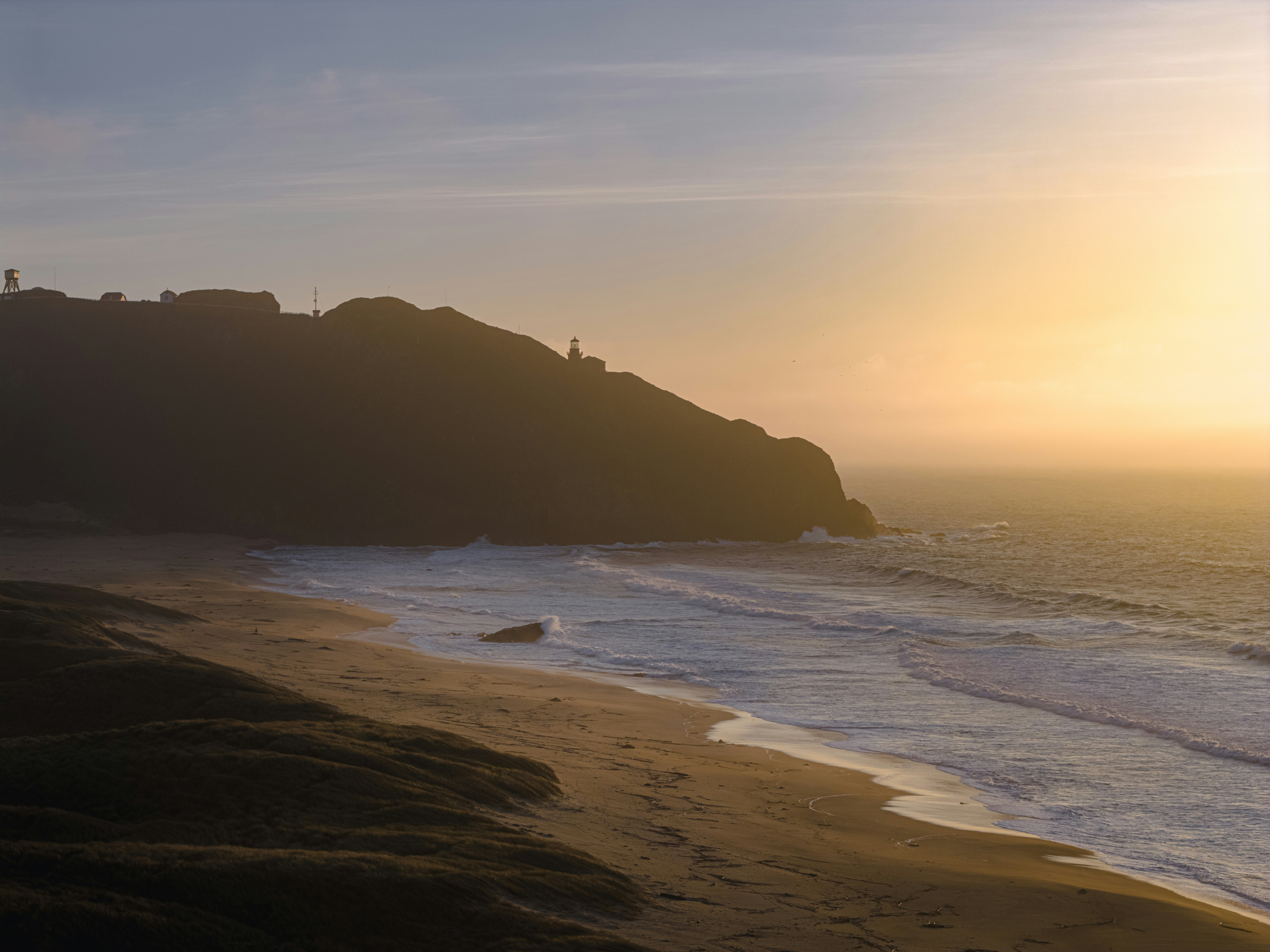 Coastal hill with lighthouse at sunset