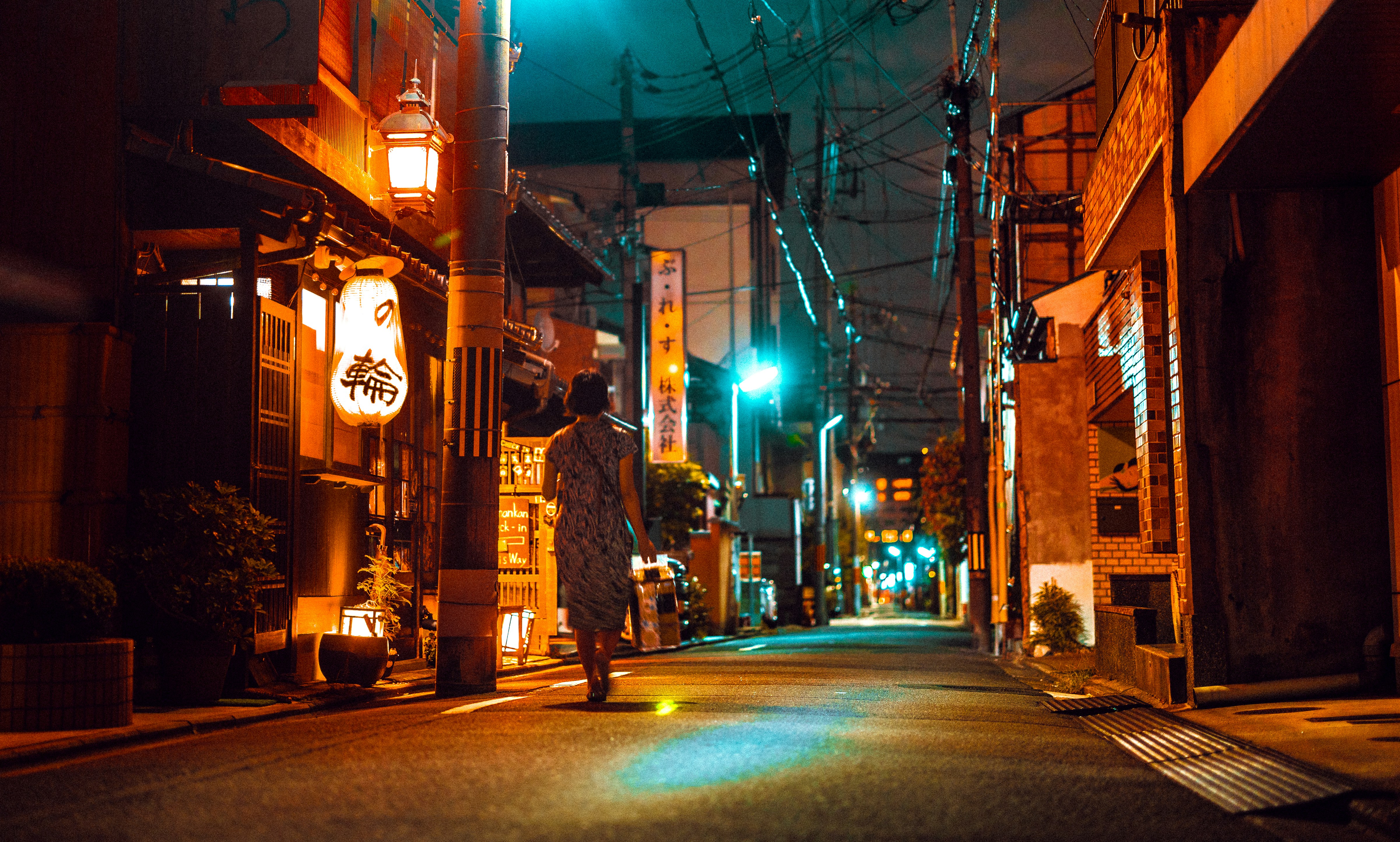 A person walks down a narrow street at night.