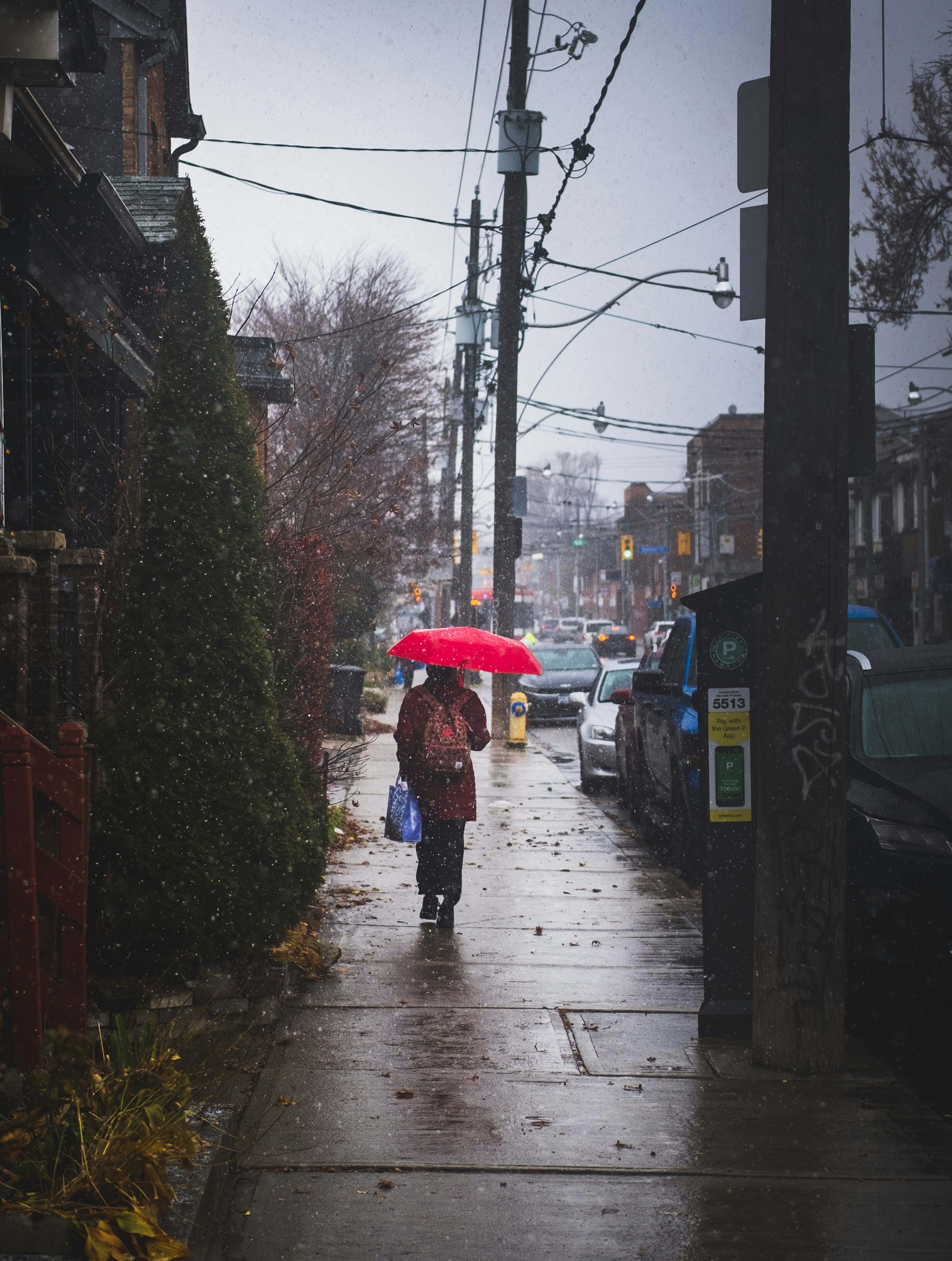 Person with red umbrella walks down rainy street