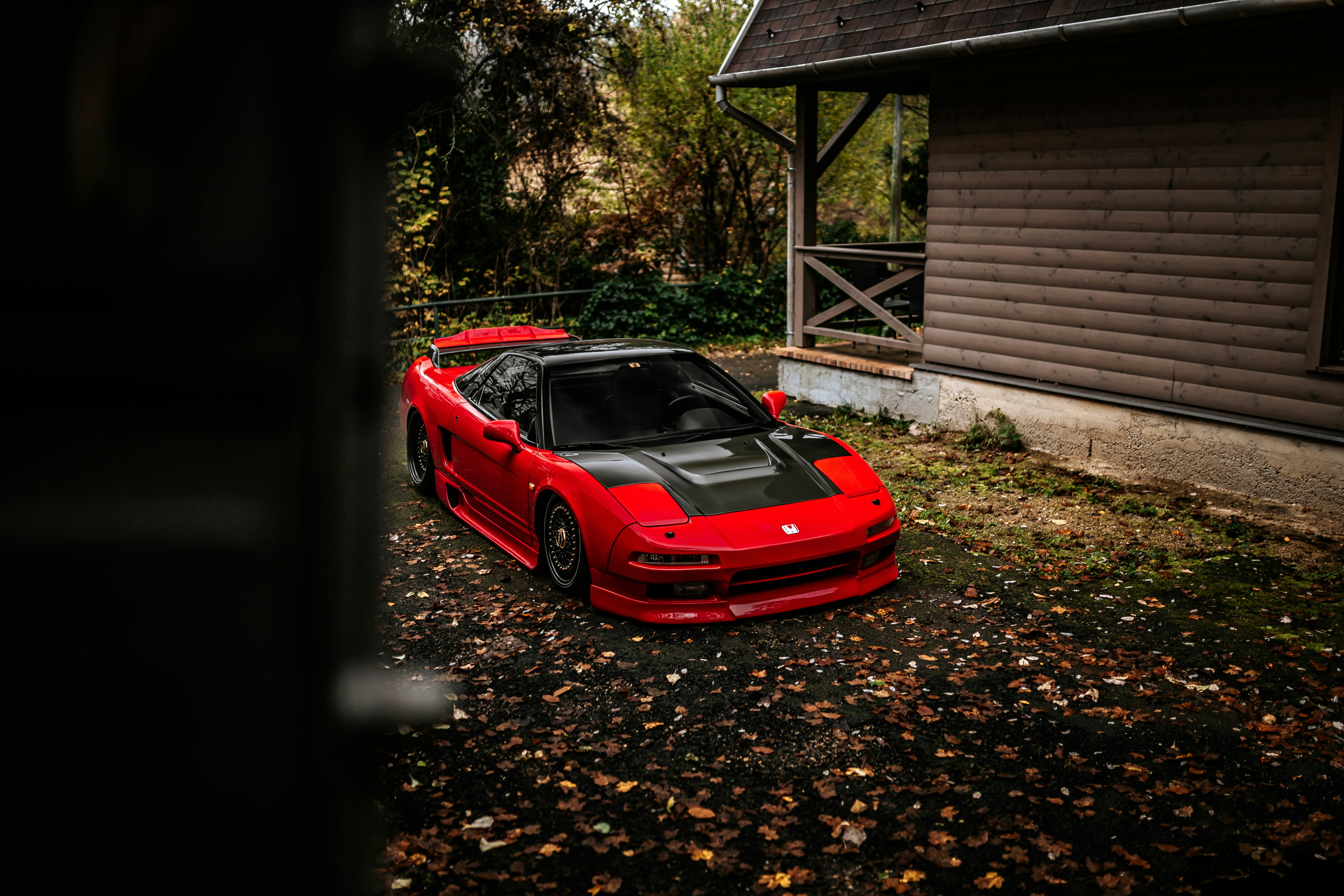 Red sports car parked near a wooden house