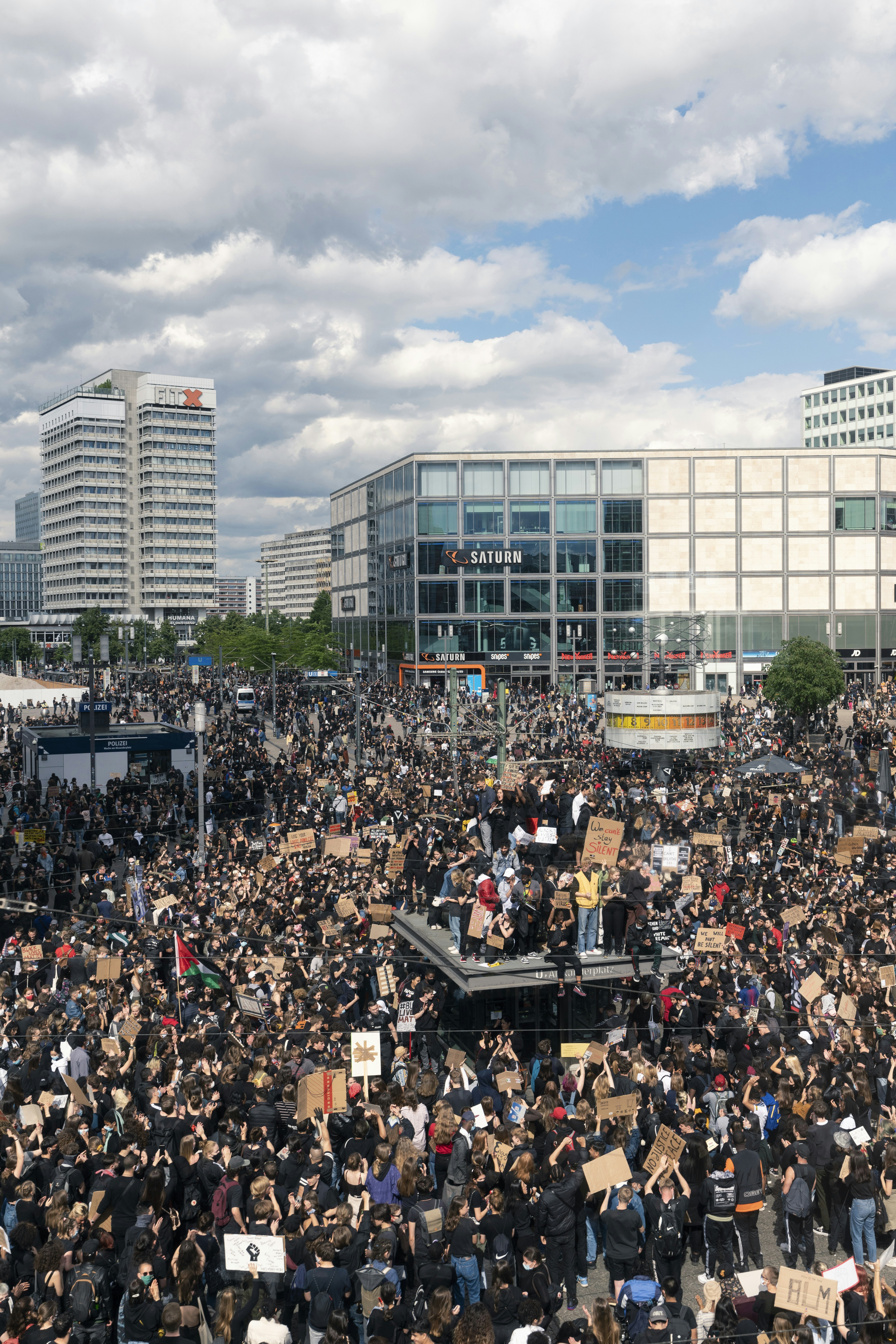 Large crowd of people gathered in urban square with signs.