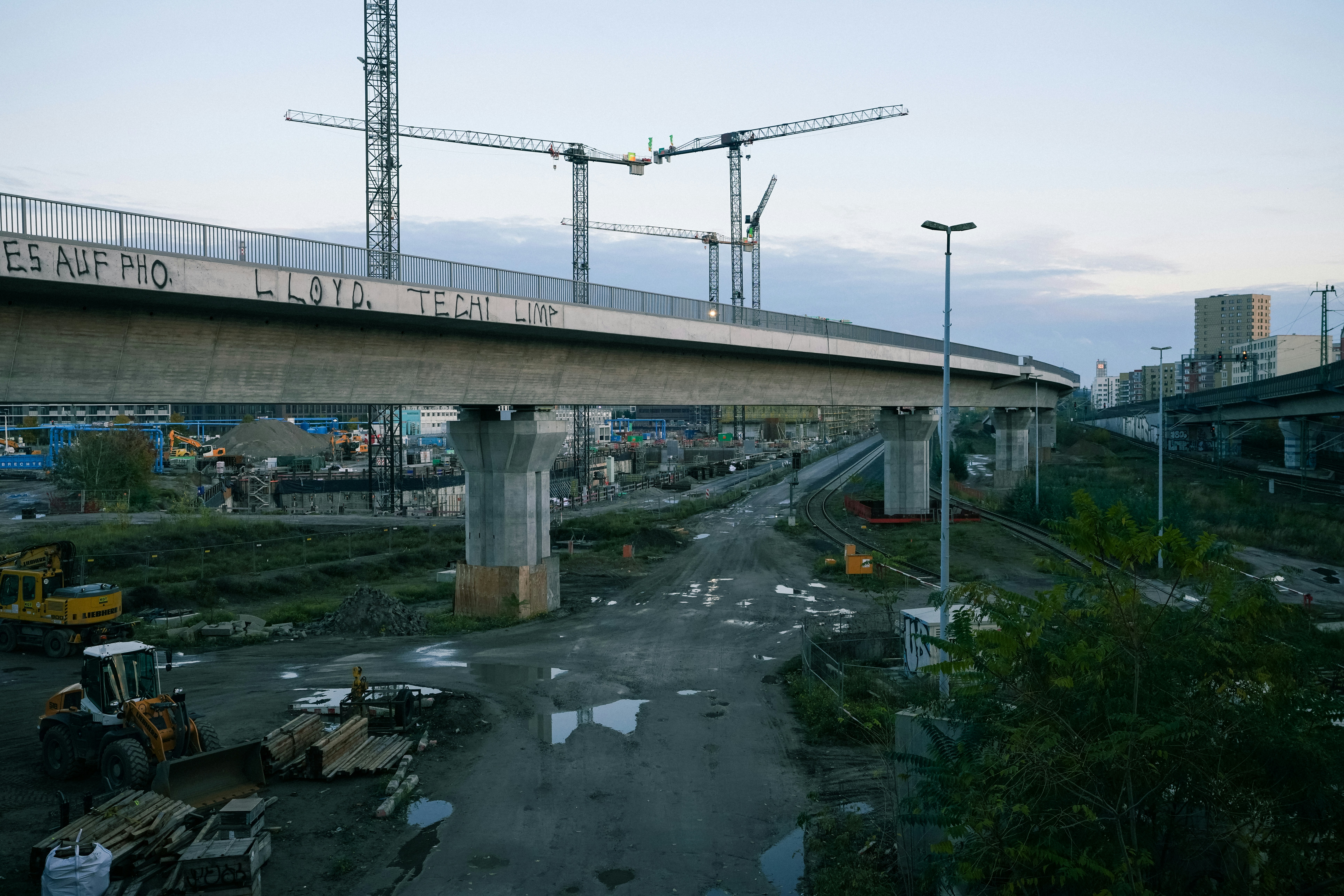 Construction site with cranes and a bridge overhead.