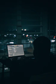 Person coding on laptop overlooking city lights at night