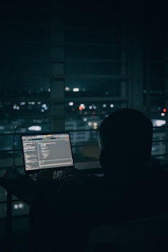 Person coding on laptop overlooking city lights at night