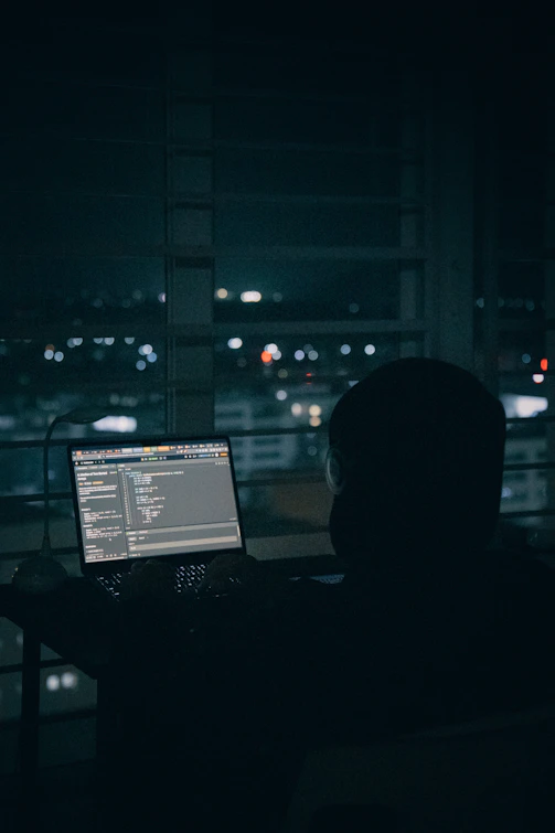 Person coding on laptop overlooking city lights at night