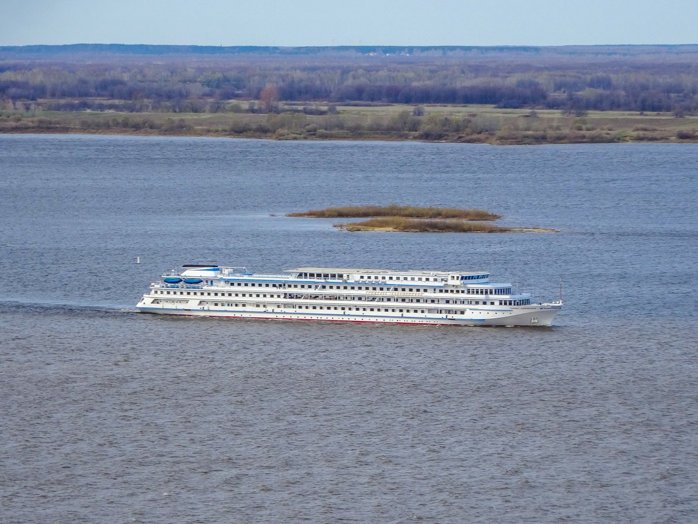 A long white river cruise ship on a wide, calm river under a pale sky