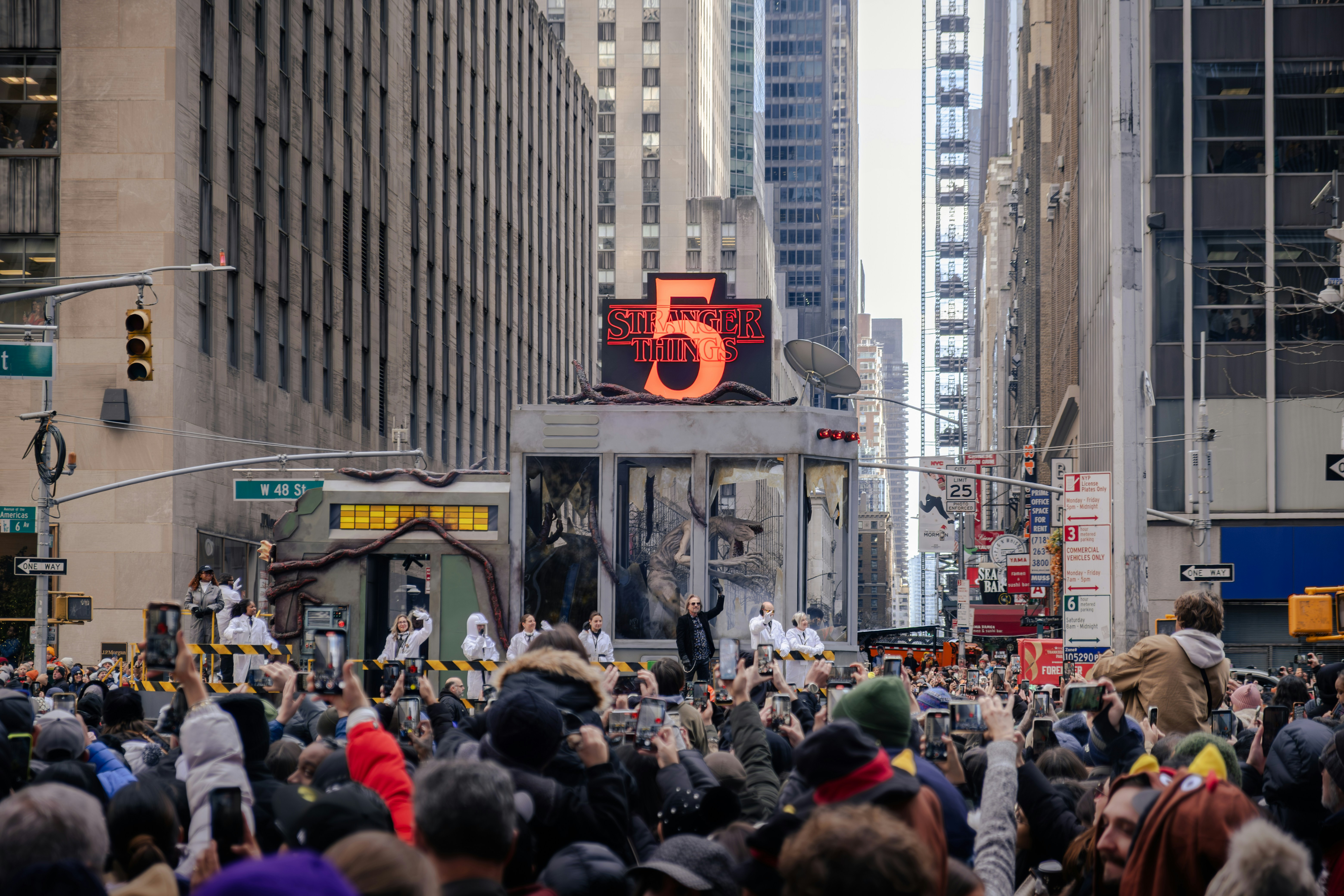Crowd watches a parade with large number 5 sign.