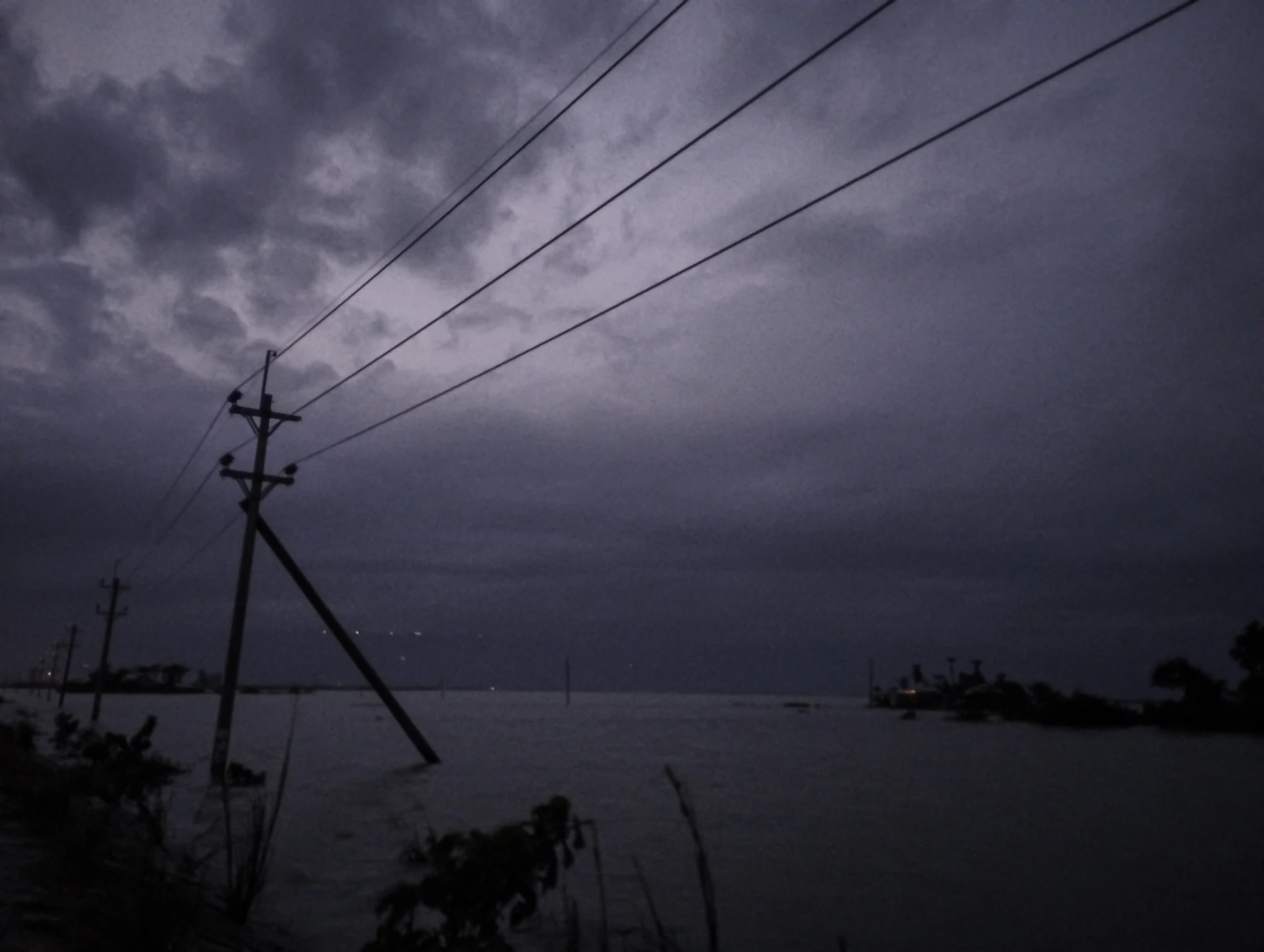 Dark stormy clouds over a flooded landscape with power lines.