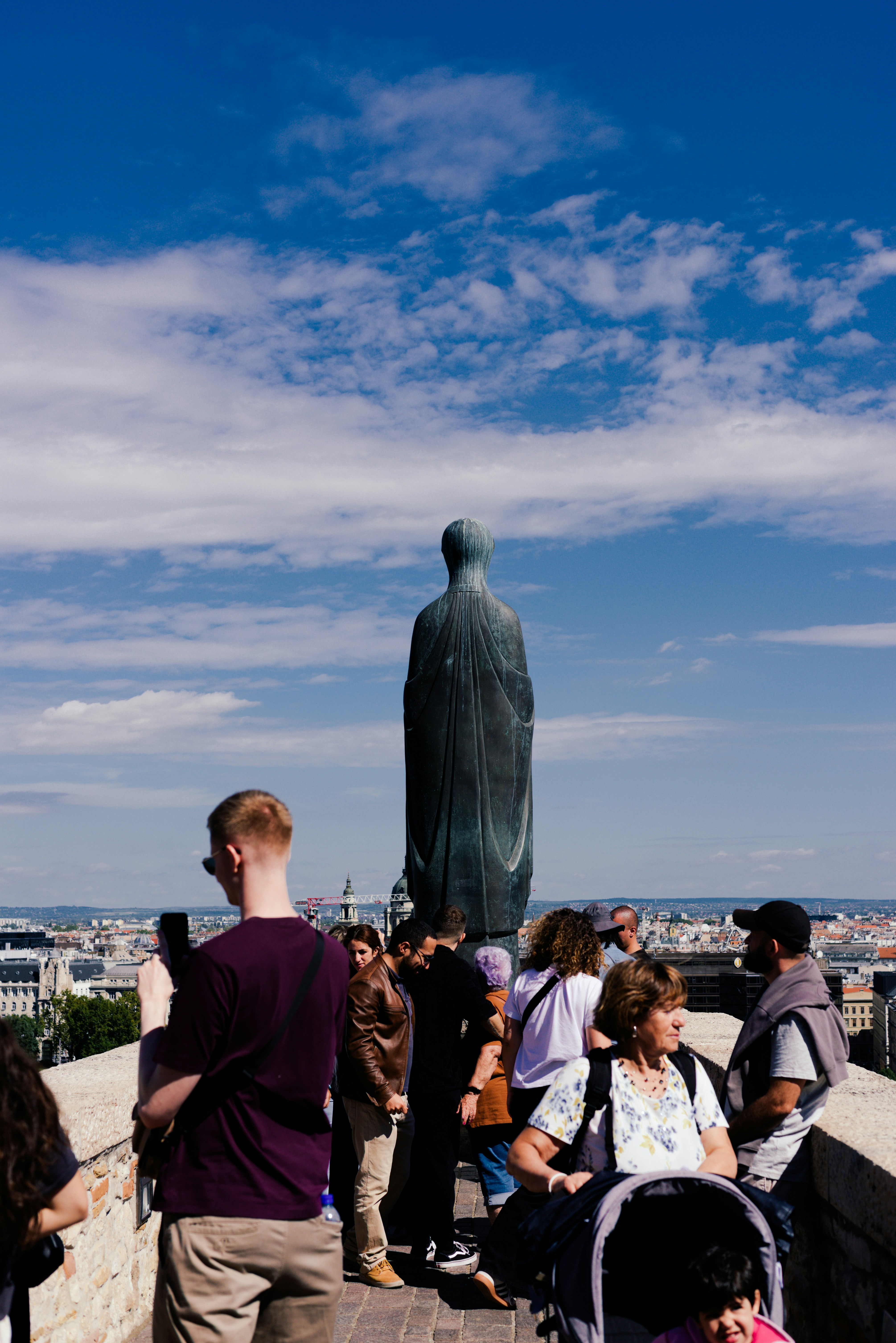 Tourists gather near a tall statue overlooking a city.