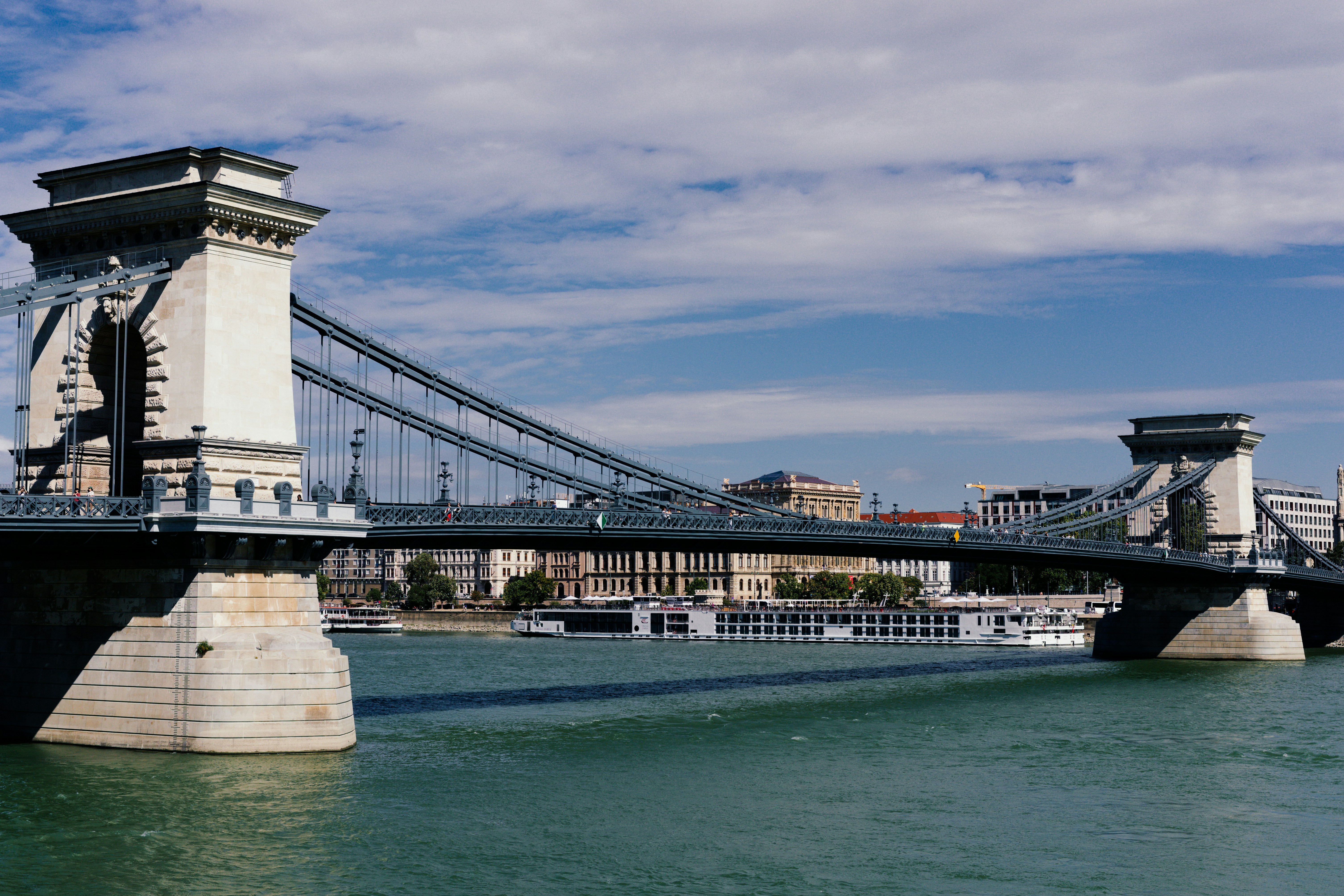 Chain bridge over a wide river with buildings