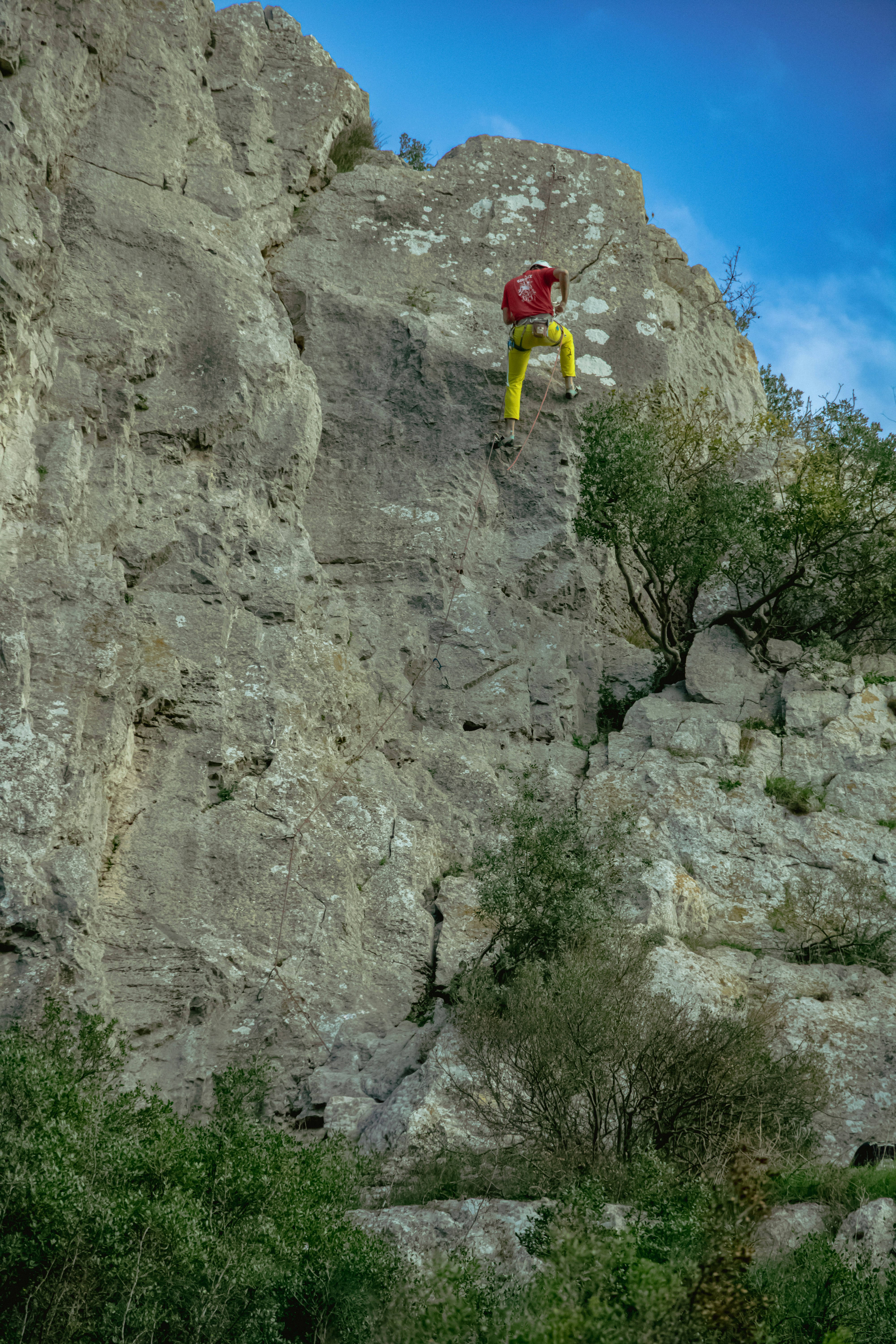 青空の下、岩だらけの崖を登るクライマーが登っています。