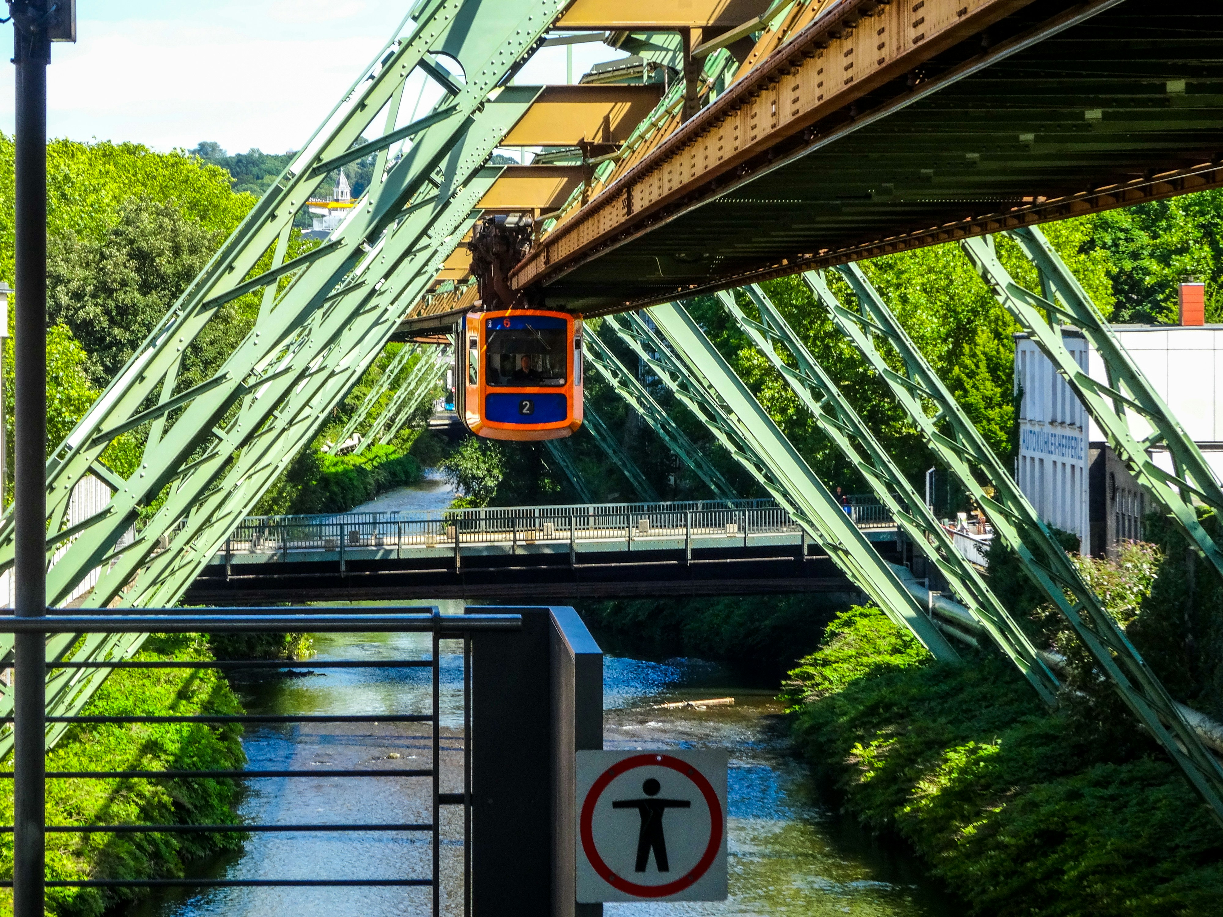 Orange suspended train over a river and green trees