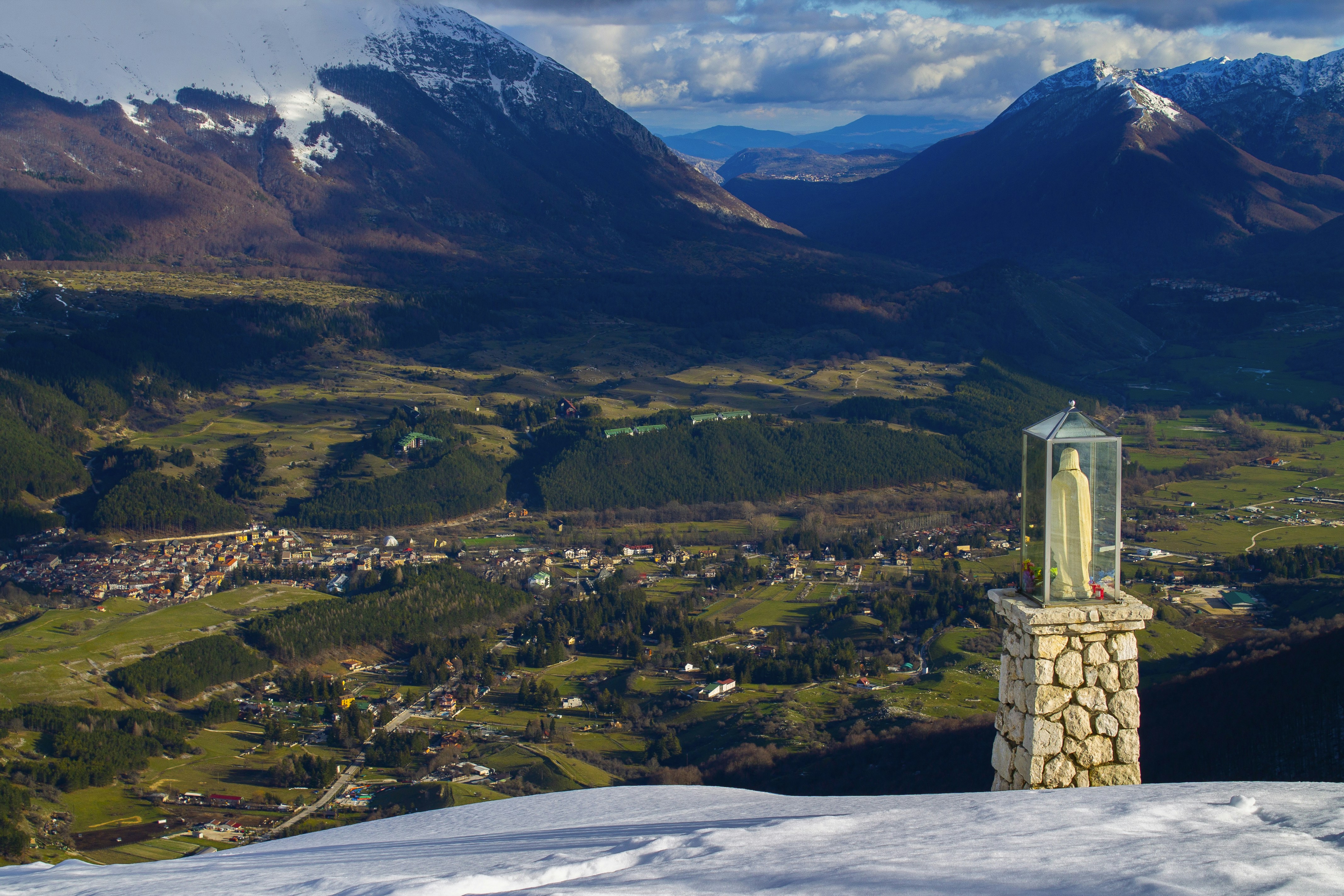 Une statue surplombe une vallée aux montagnes lointaines.