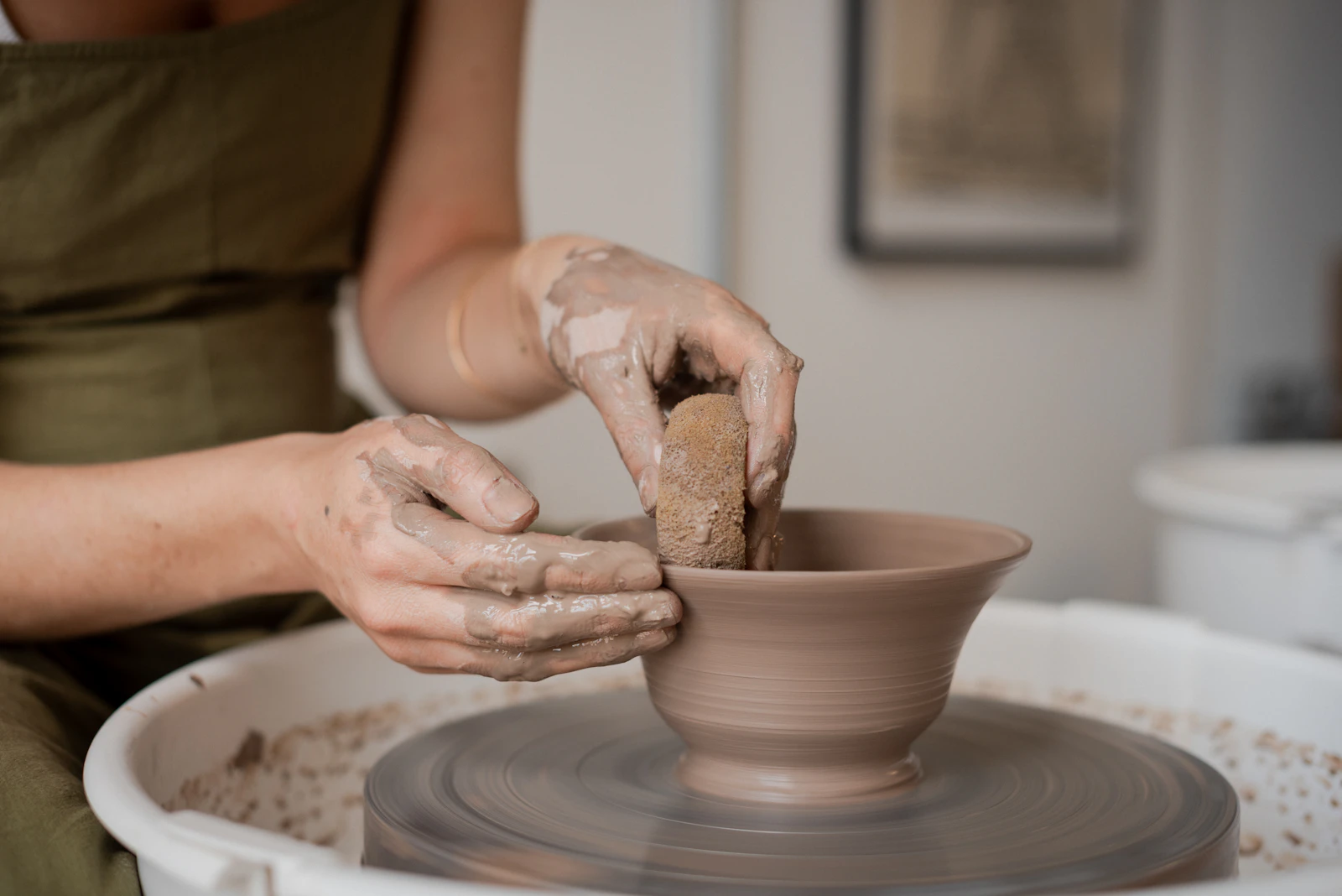 Hands centring and pulling up wet clay on a traditional potter's wheel