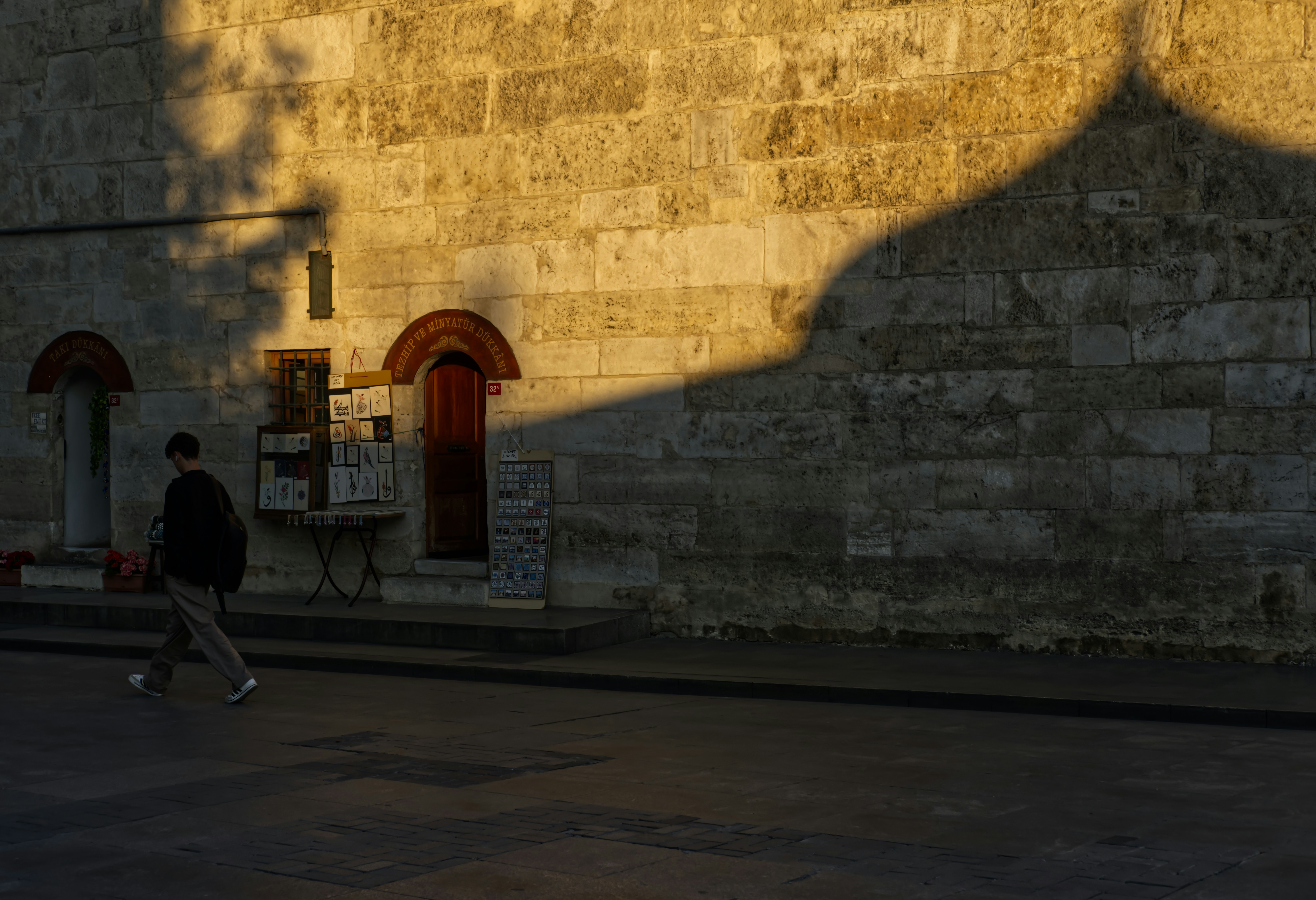 Man walks past stone building with arched doorways at sunset.