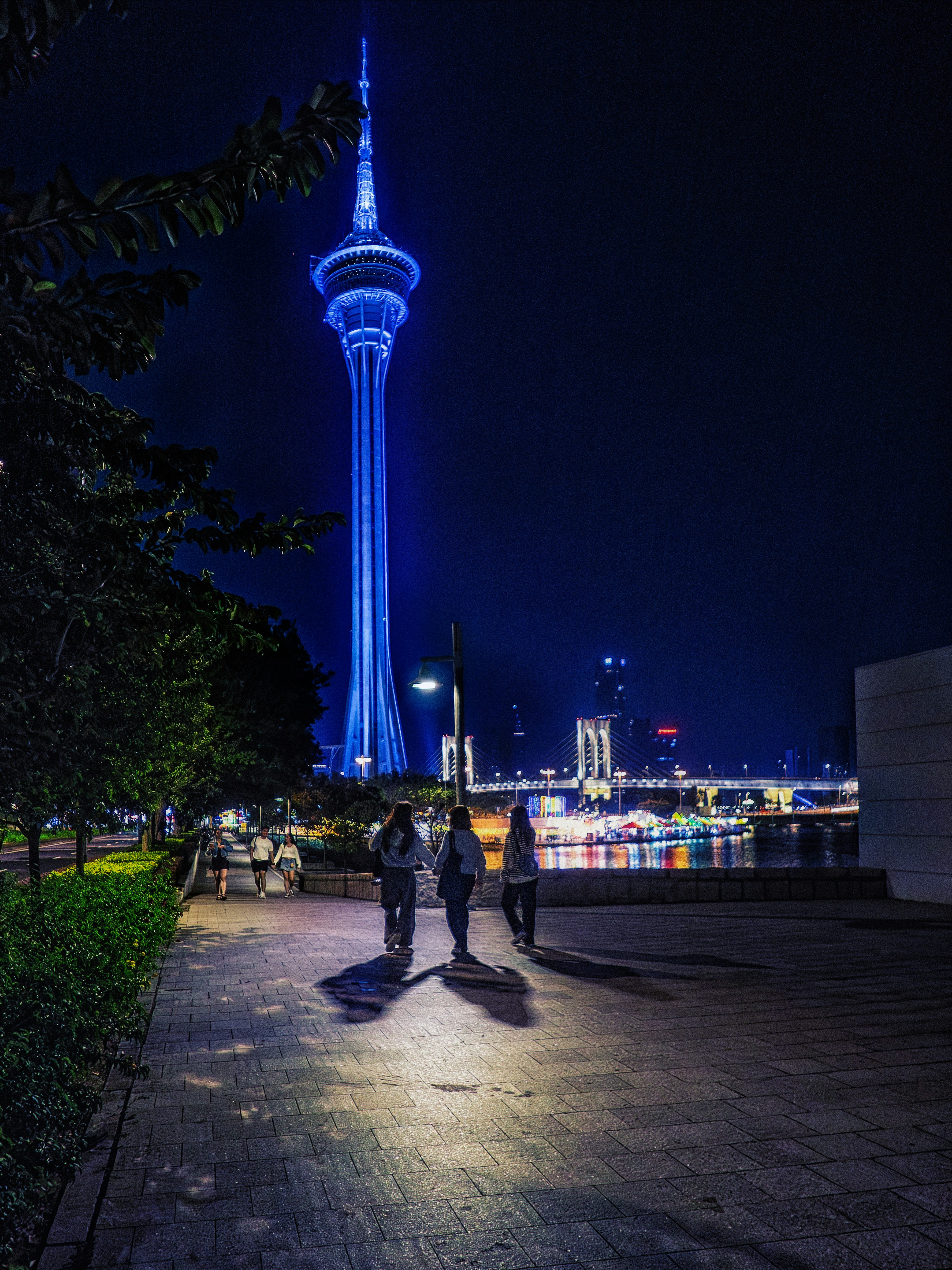 Three people walk towards a brightly lit tower at night.