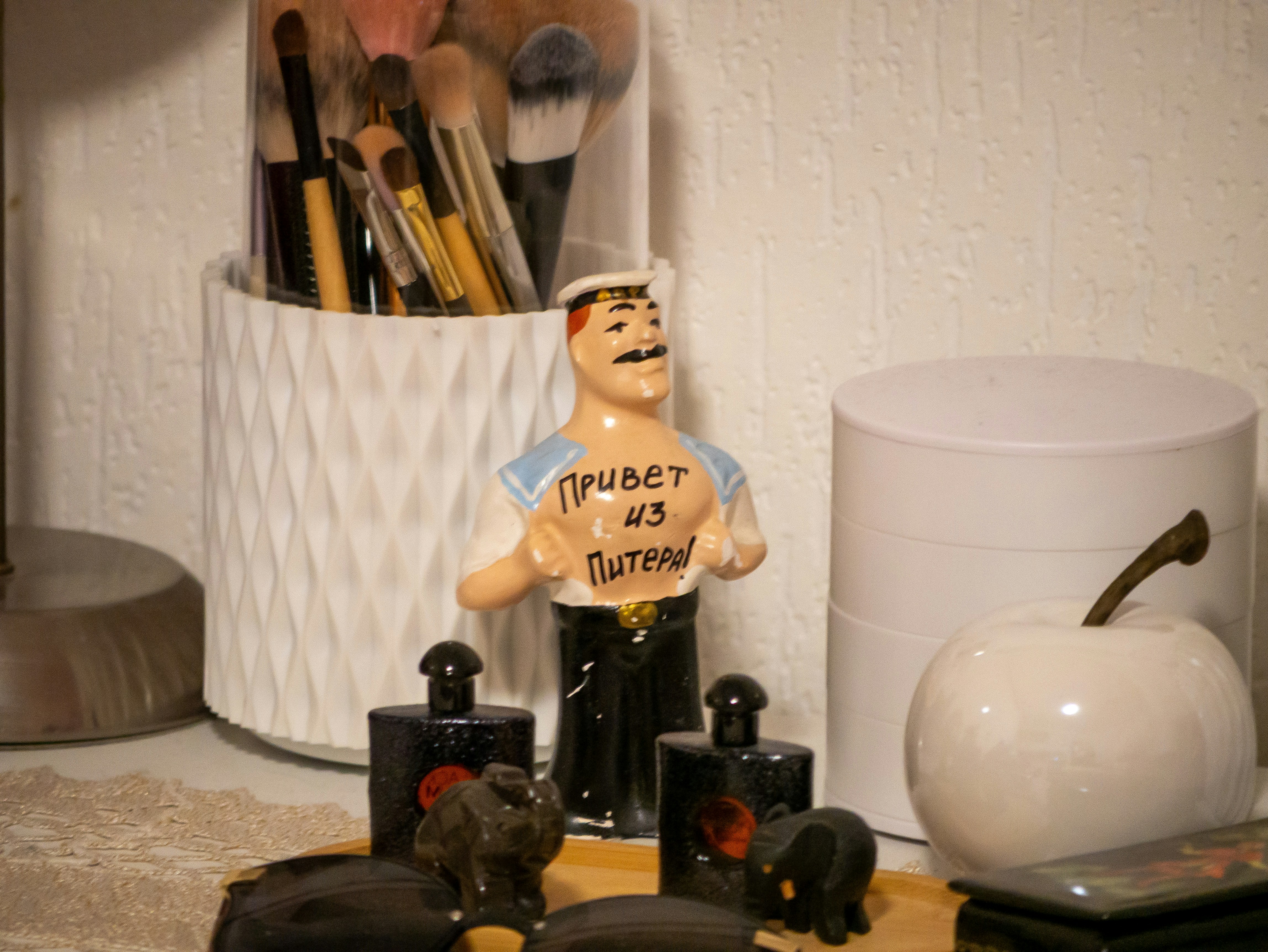 Figurine with russian text near perfume bottles and makeup brushes.