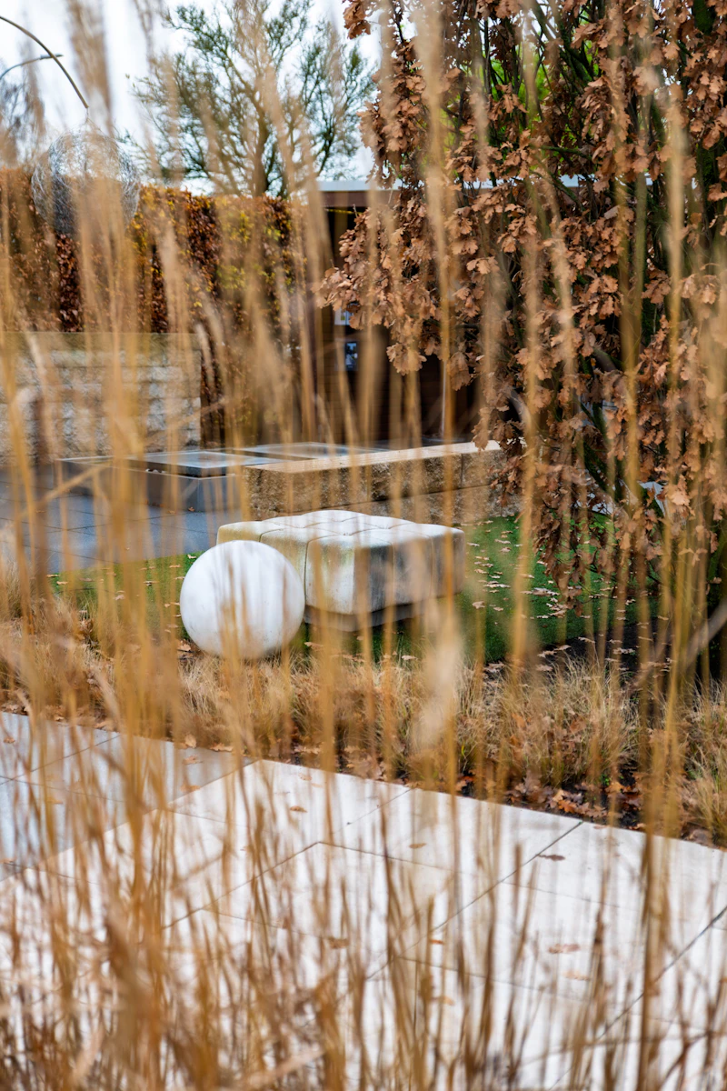Steinbank und Kugelskulptur zwischen Ziergräsern in einem modernen Garten