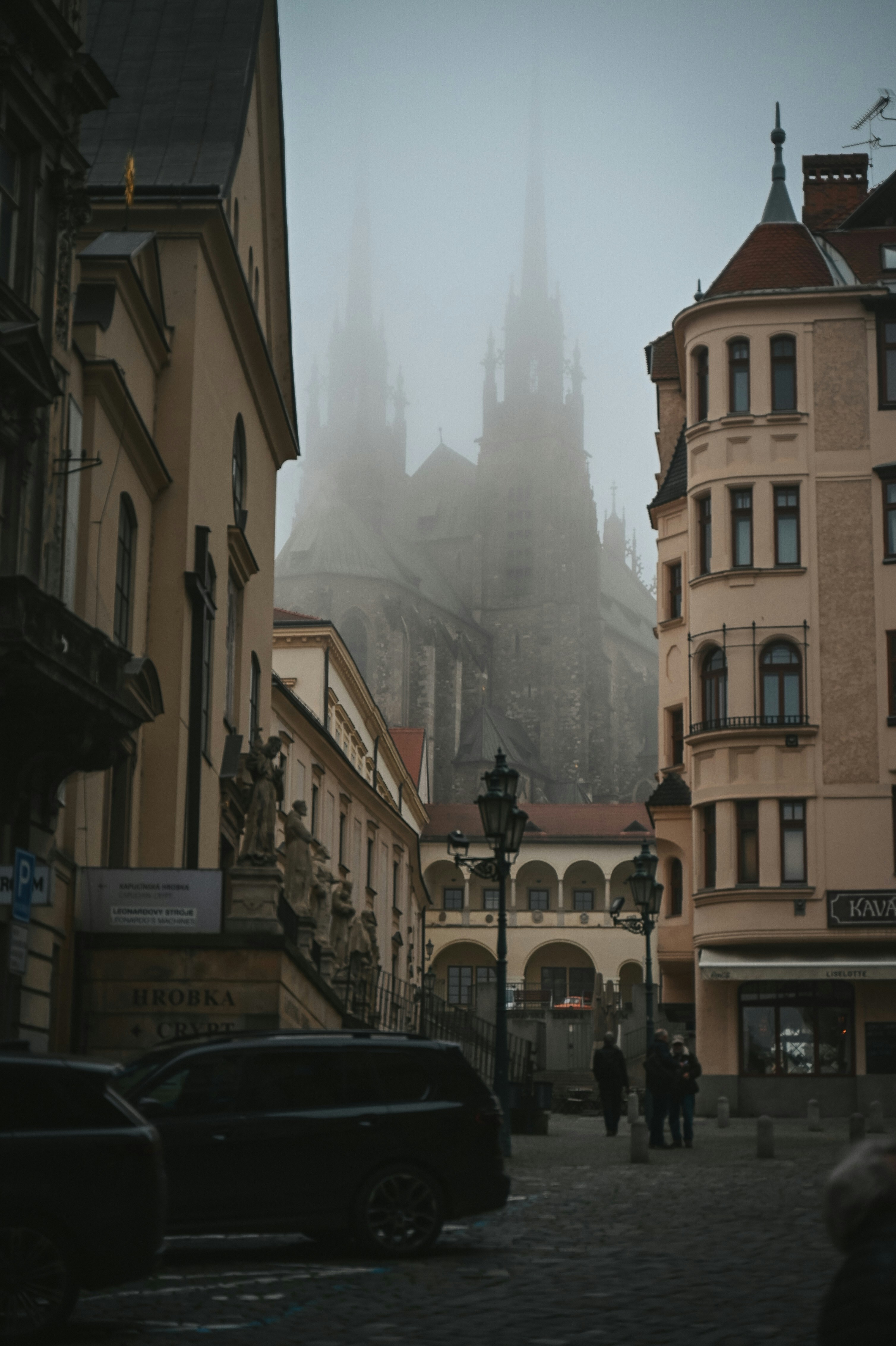 Calle de la ciudad con niebla y una catedral gótica al fondo.
