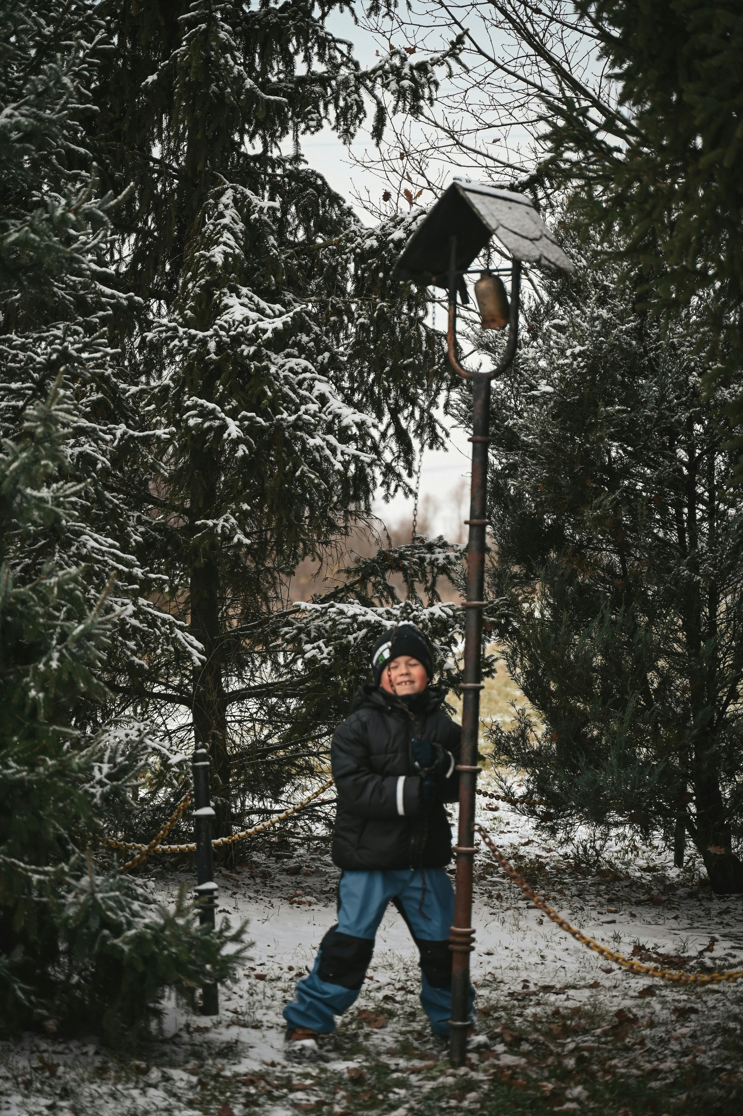 Niño joven de pie junto a un viejo farol en un bosque nevado.