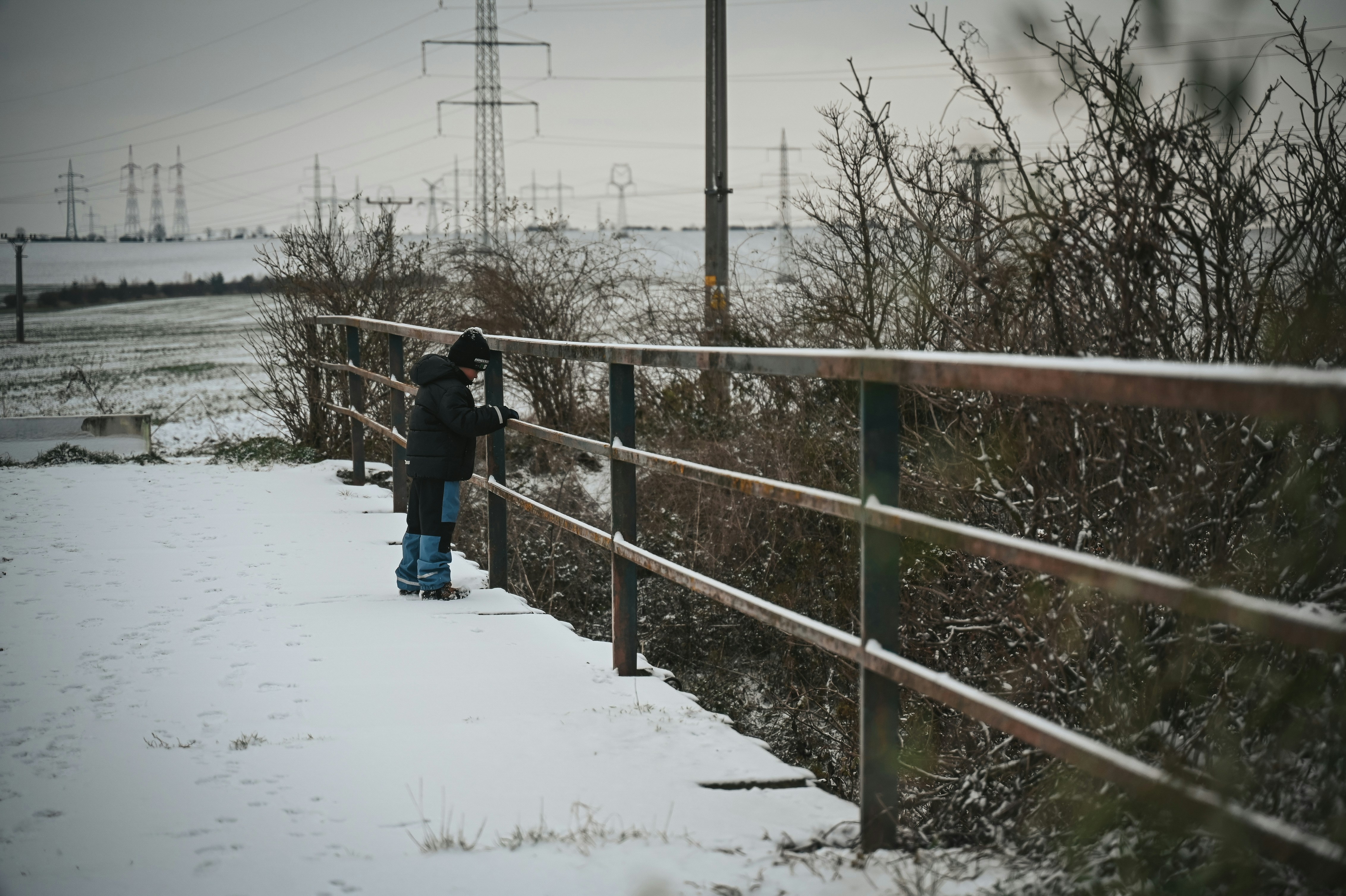 Niño con abrigo de invierno apoyado en una valla de madera