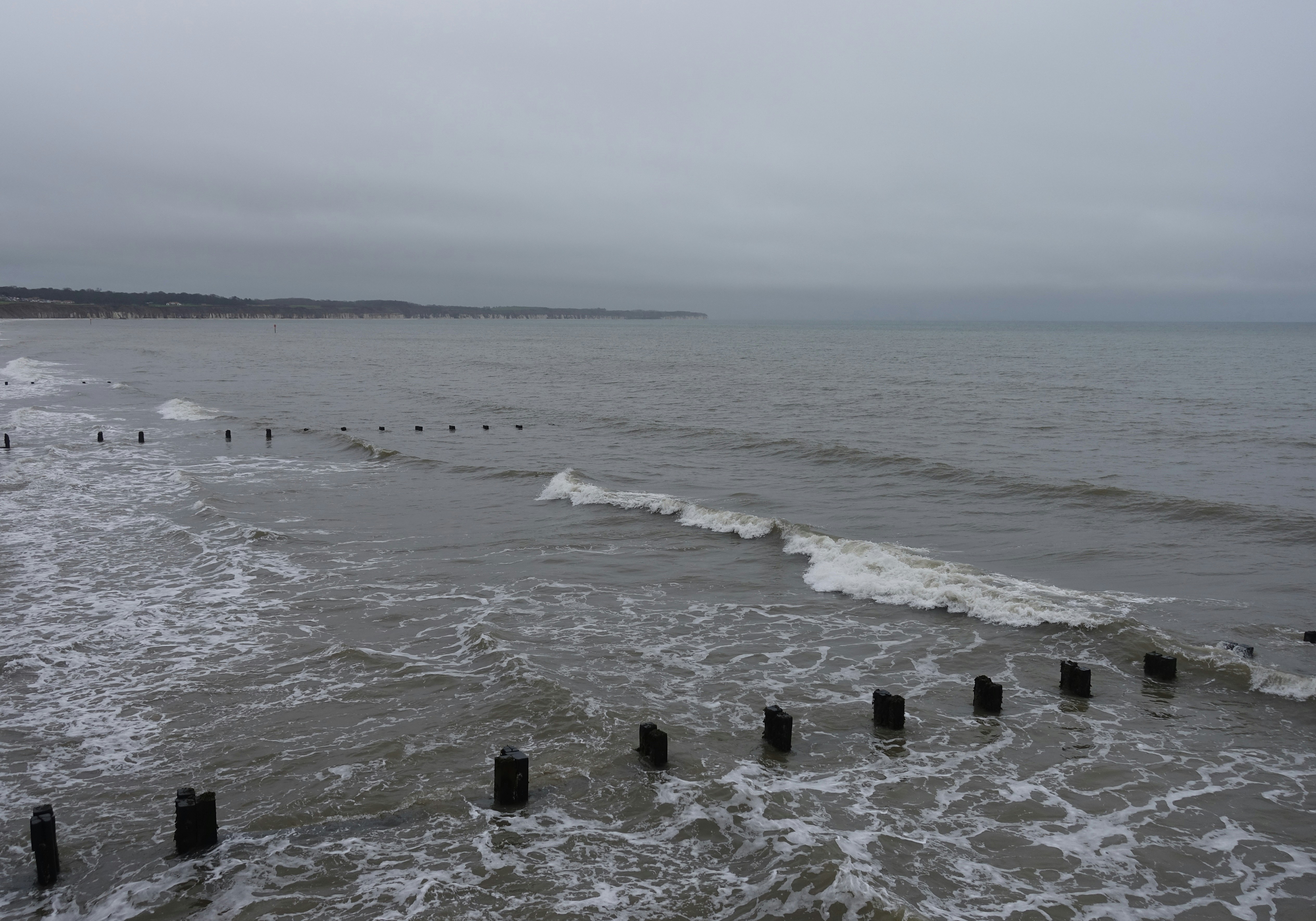 Waves crashing on a beach with wooden posts.