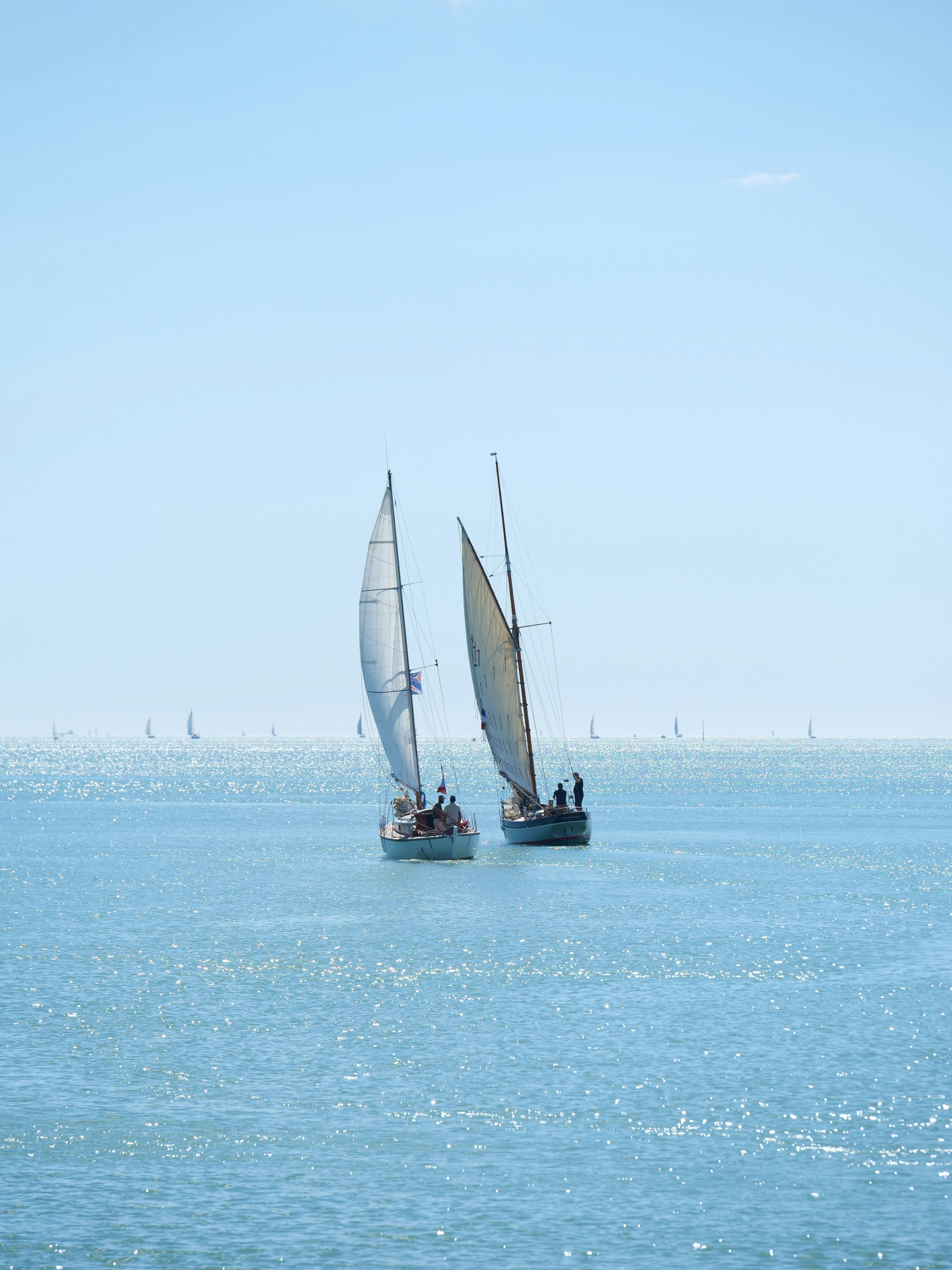 Two sailboats race on a clear blue day.