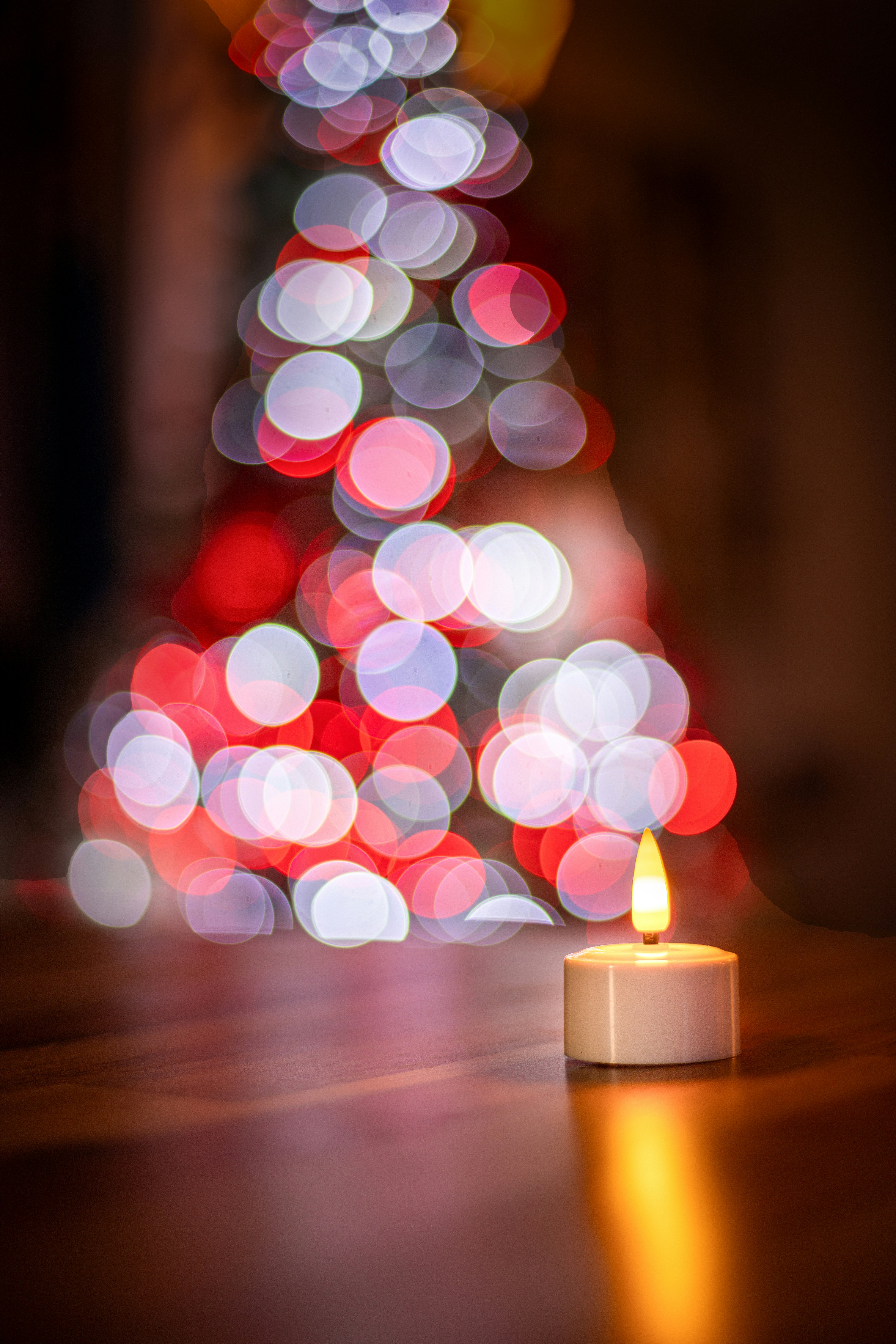 A lit candle in front of blurred christmas tree lights.