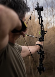 Man aiming a compound bow and arrow outdoors