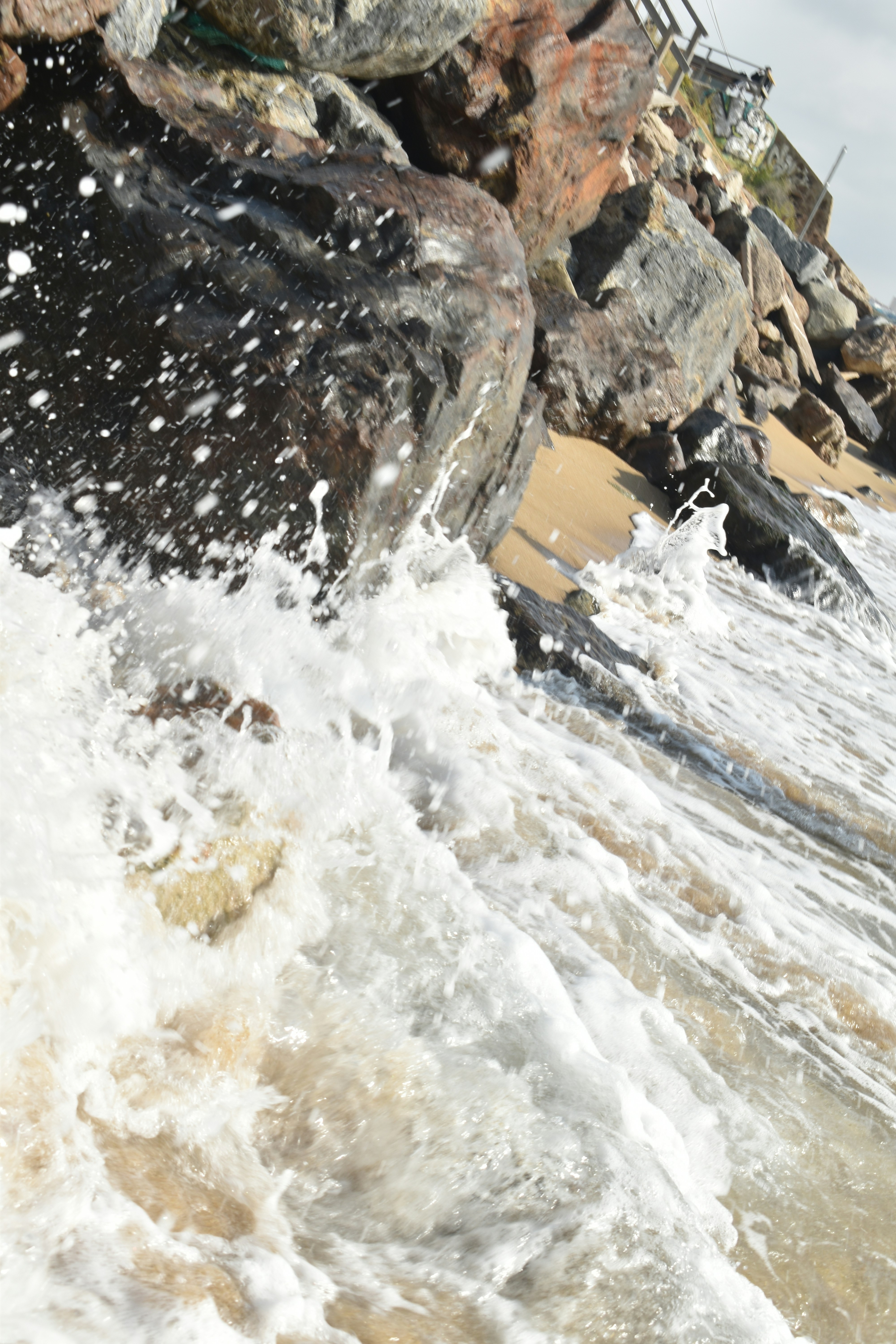 Waves crashing against large rocks on a sandy beach.