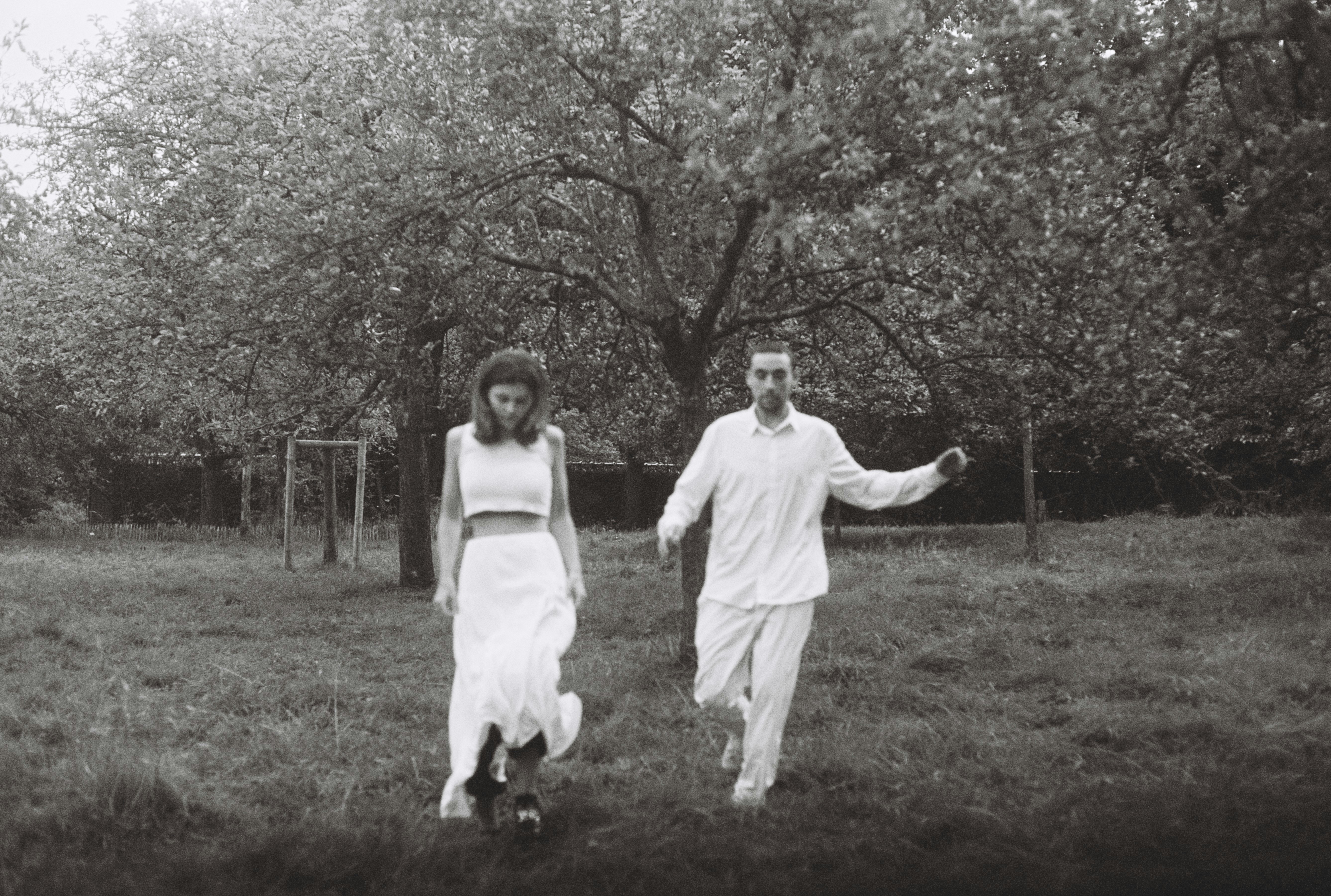 A couple in white running through a field.