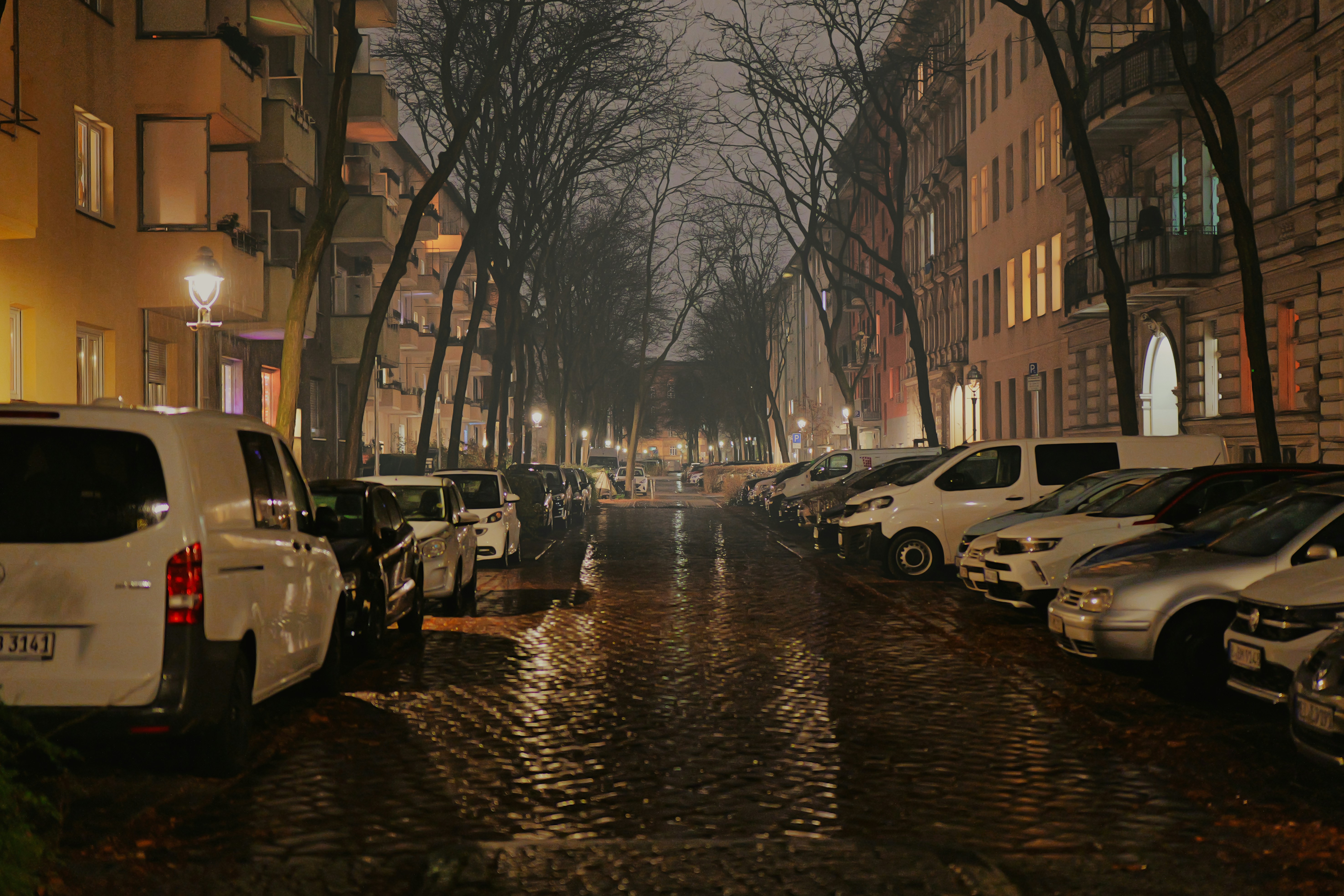 Rainy street lined with parked cars and buildings at night. - rainy-street-lined-with-parked-cars-and-buildings-at-night-R_ET4rpRAWo