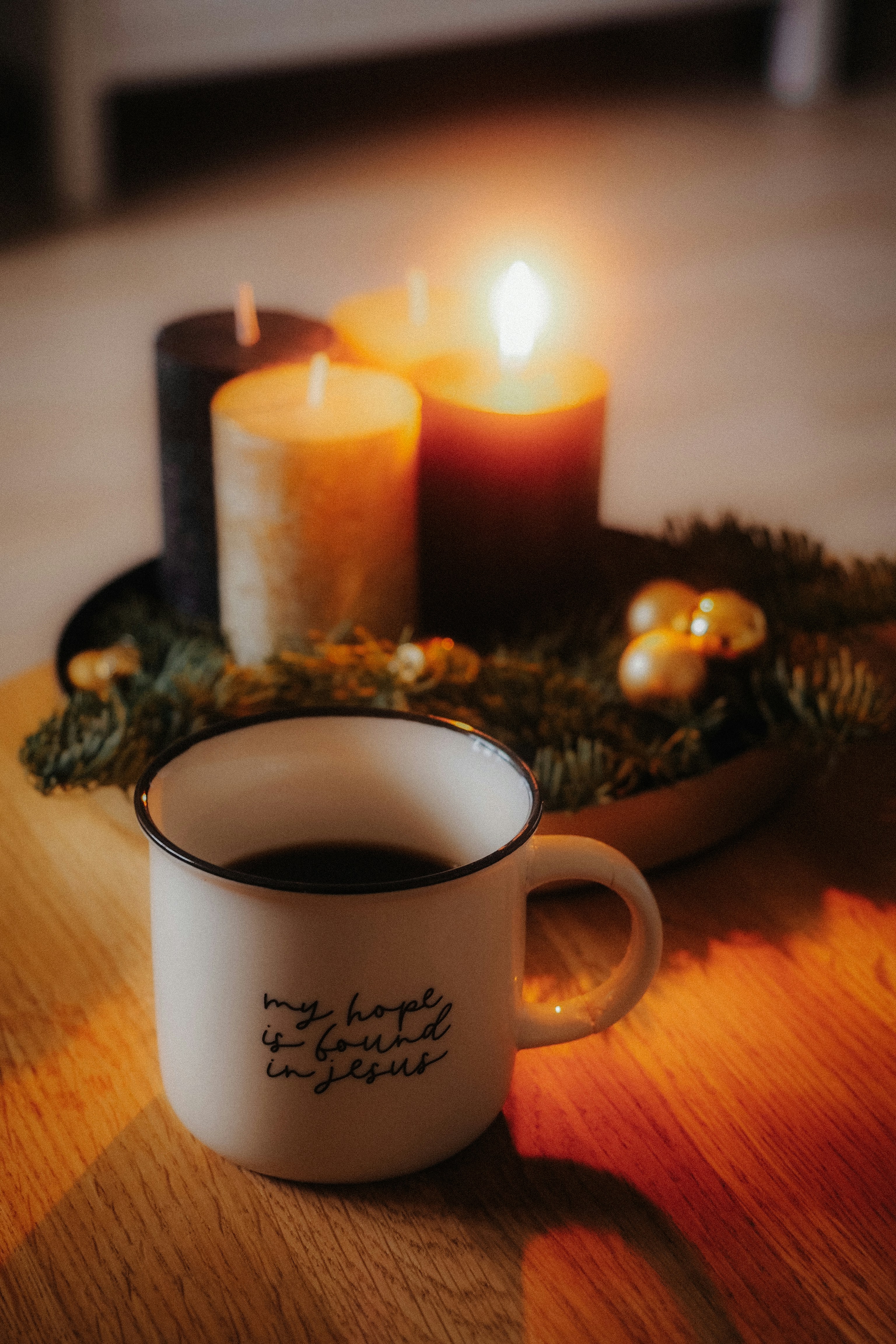A mug of coffee sits before lit advent candles.