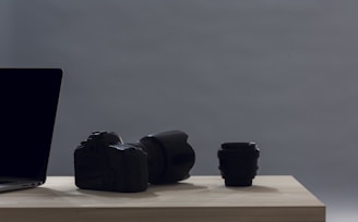 A laptop, camera, and lens on a wooden table.