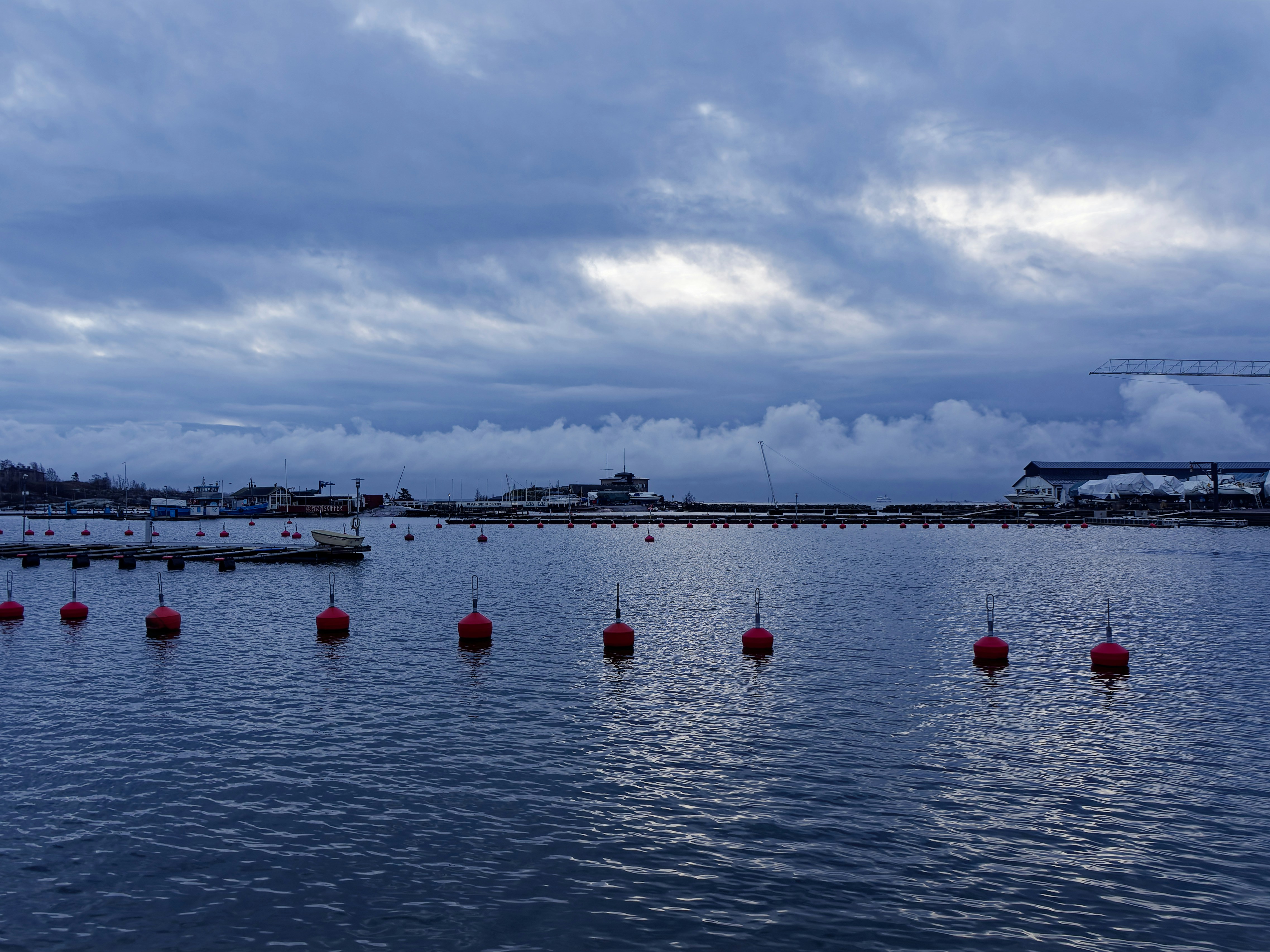 Red buoys float on the water under cloudy skies.