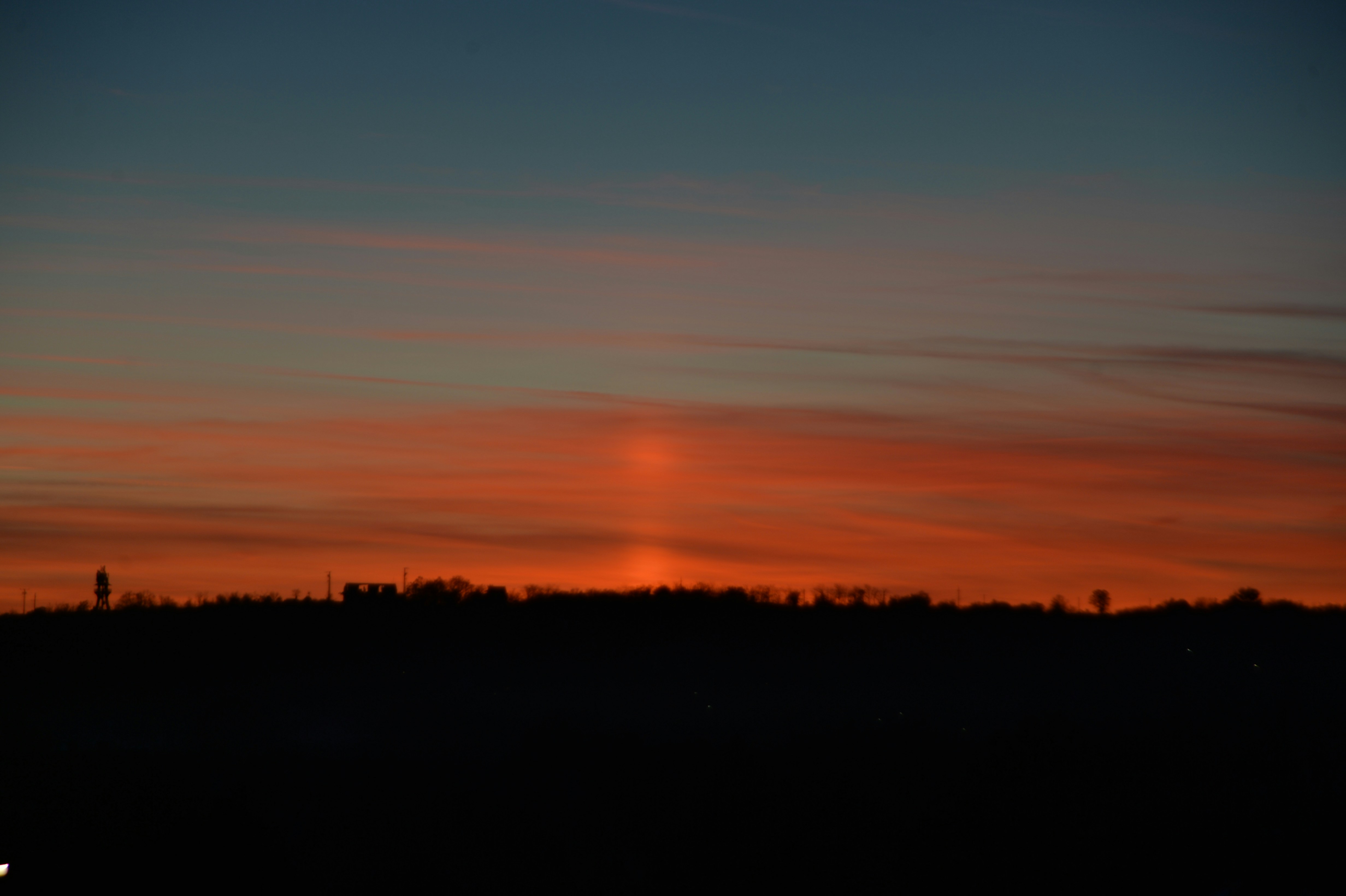 Sunset over a dark silhouette of trees.