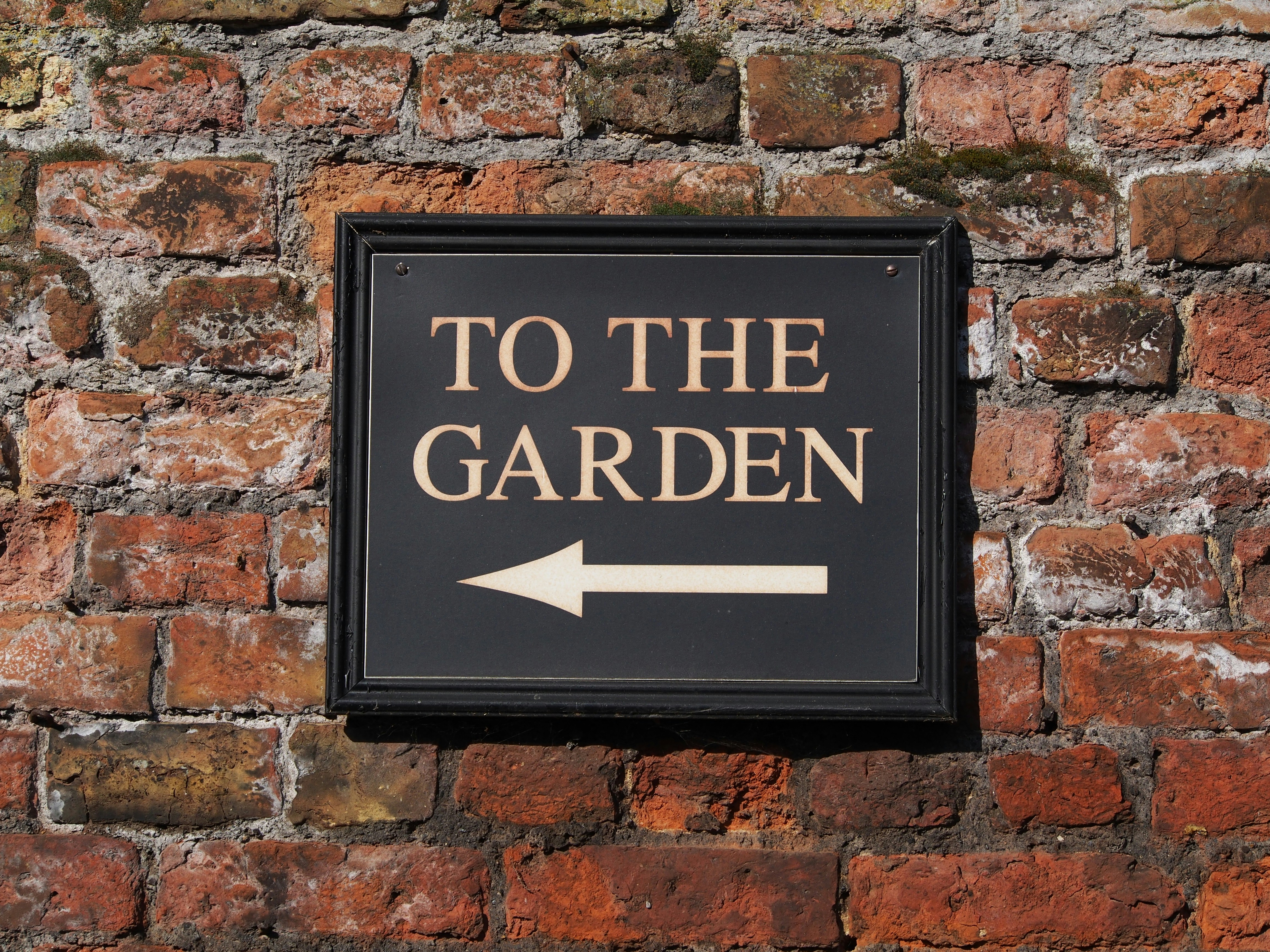 Sign pointing to the garden on brick wall