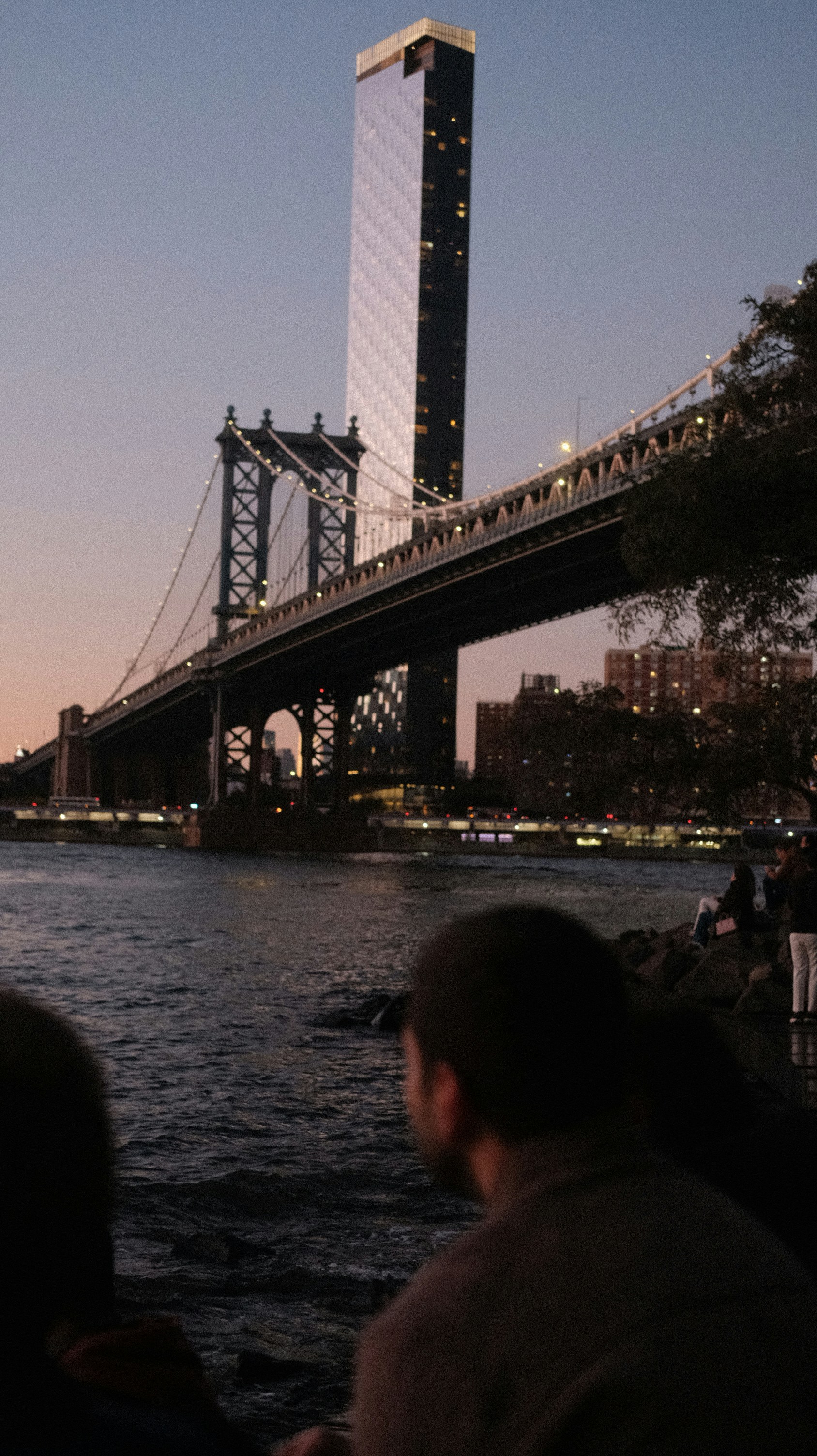 Bridge and skyscraper at dusk with people watching.
