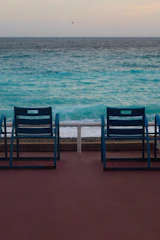 Two empty chairs face the turquoise ocean waves.
