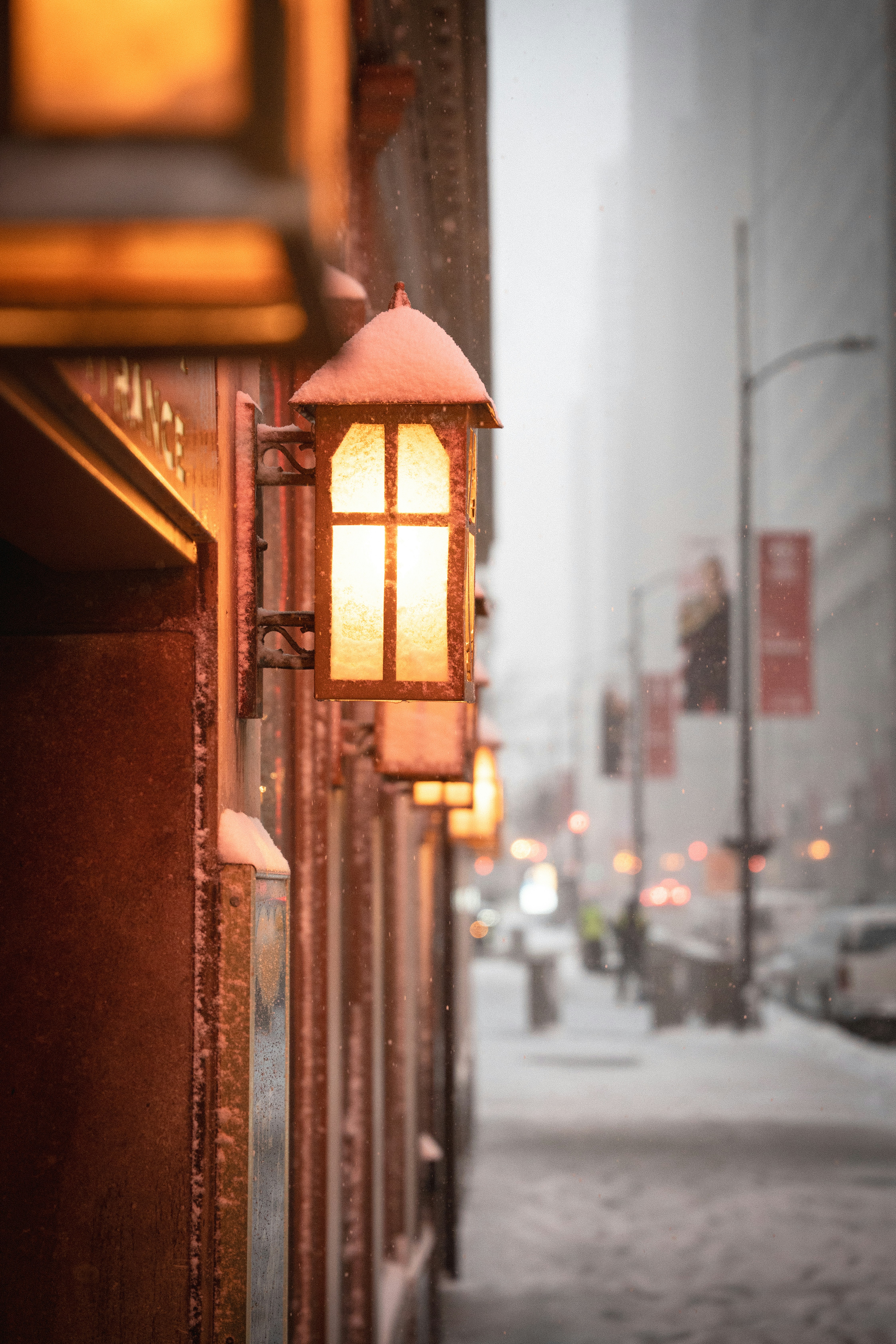 Street lamps glow on a snowy city sidewalk