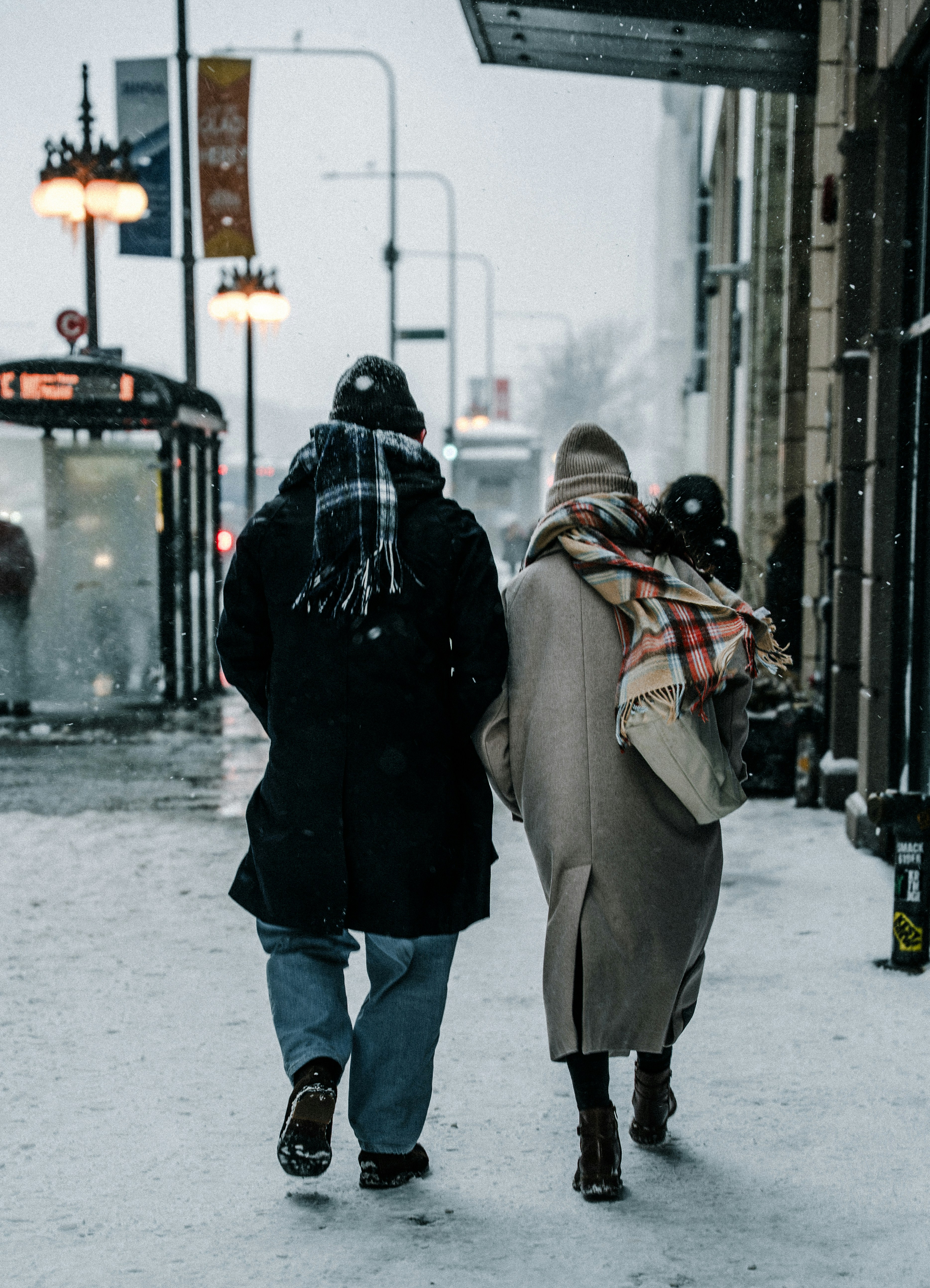Two people walk down a snowy city street.