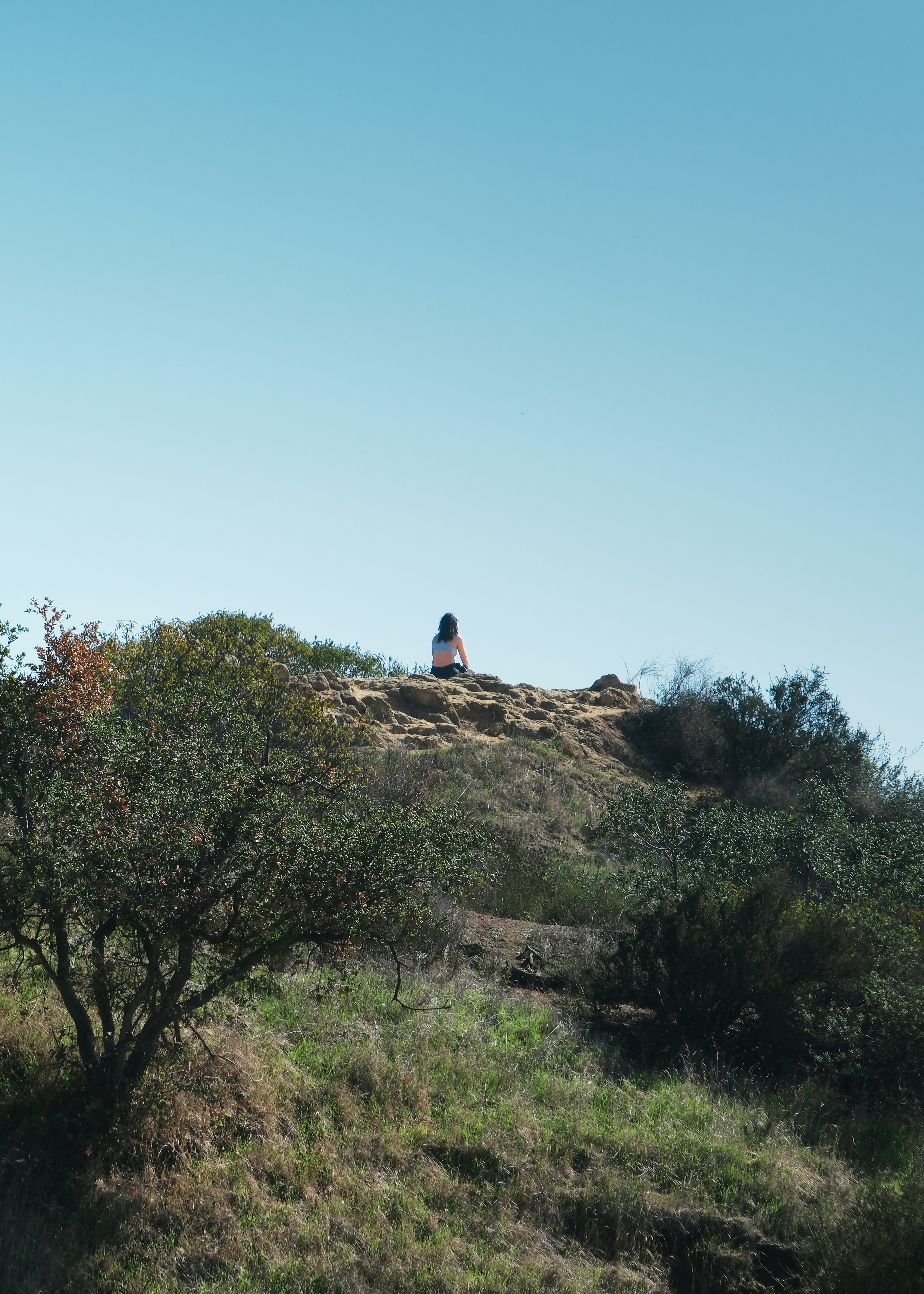 Una persona siede su una collina rocciosa che domina una valle.