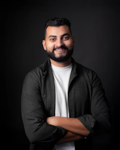 A smiling man with arms crossed against a dark background